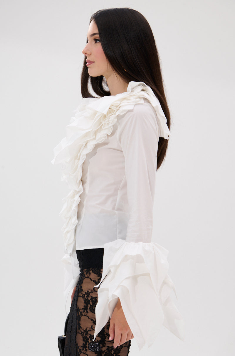 A woman with long dark hair stands in profile against a white background, wearing the OVER THE TOP RUFFLE BLOUSE featuring a high collar and dramatic sleeves, paired with a black lace skirt. 2