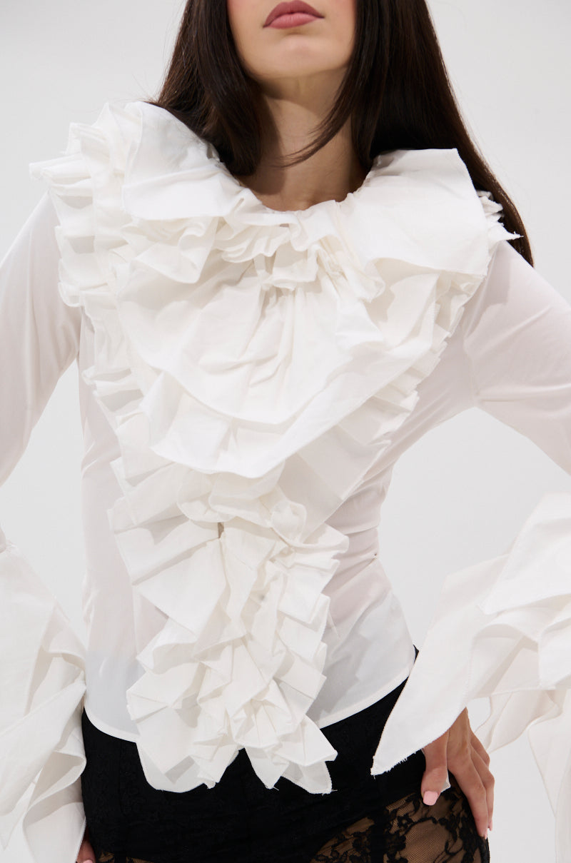 A woman wears the OVER THE TOP RUFFLE BLOUSE, a sheer white high-collar top with dramatic ruffled details on the chest and sleeves, paired with black lace bottoms. Her face is partially out of frame. 6