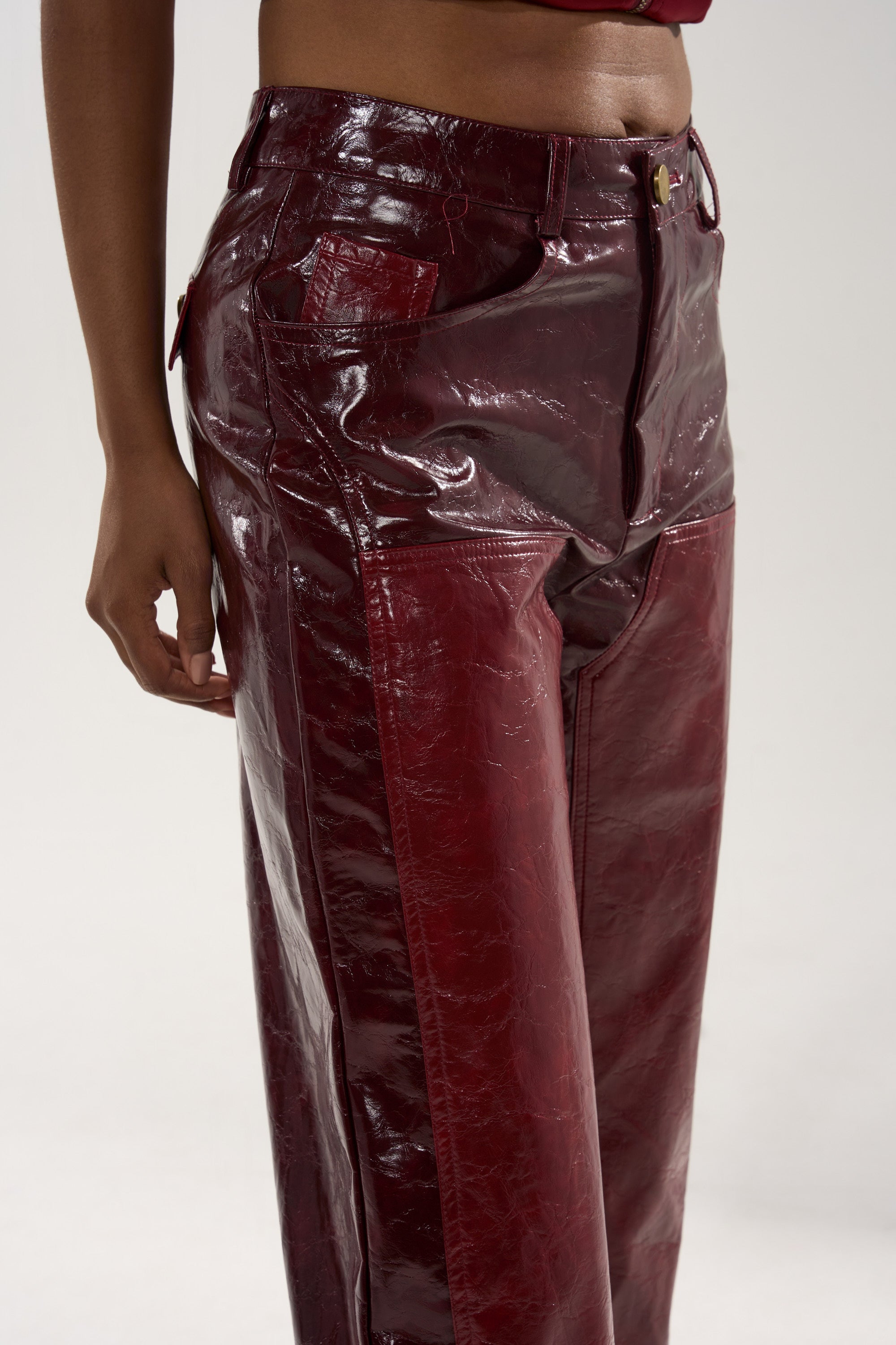Model wears MIXED EMOTIONS FAUX LEATHER TROUSER in high-rise, glossy burgundy faux leather with a matching crop top. Captured from mid-torso to mid-thigh against a plain background, the sleek straight-leg silhouette stands out.