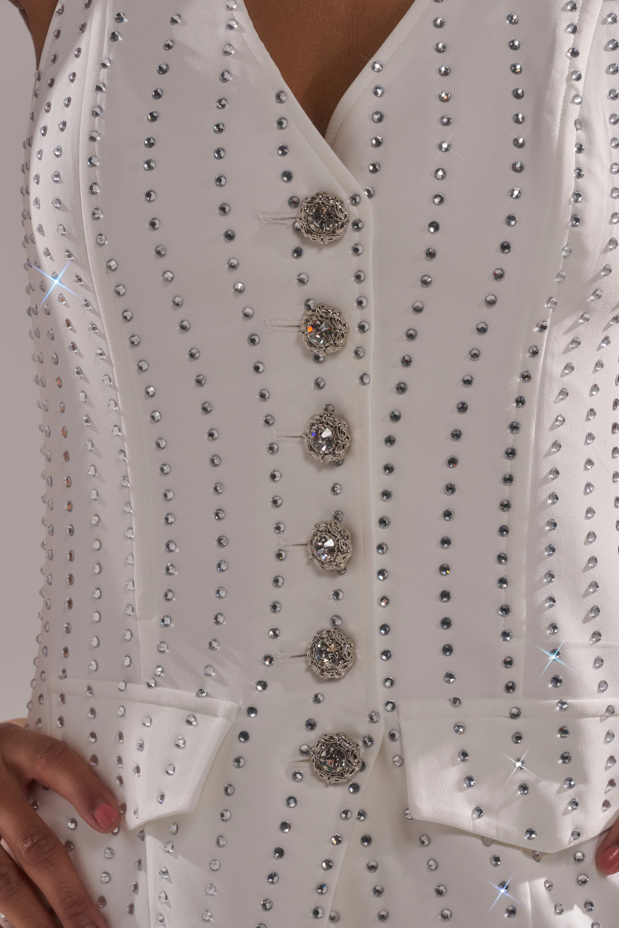 A close-up of the NEW YEARS QUEEN VEST IN WHITE, featuring rows of small silver studs and ornate crystal buttons, worn by a person with one hand on their hip. 6