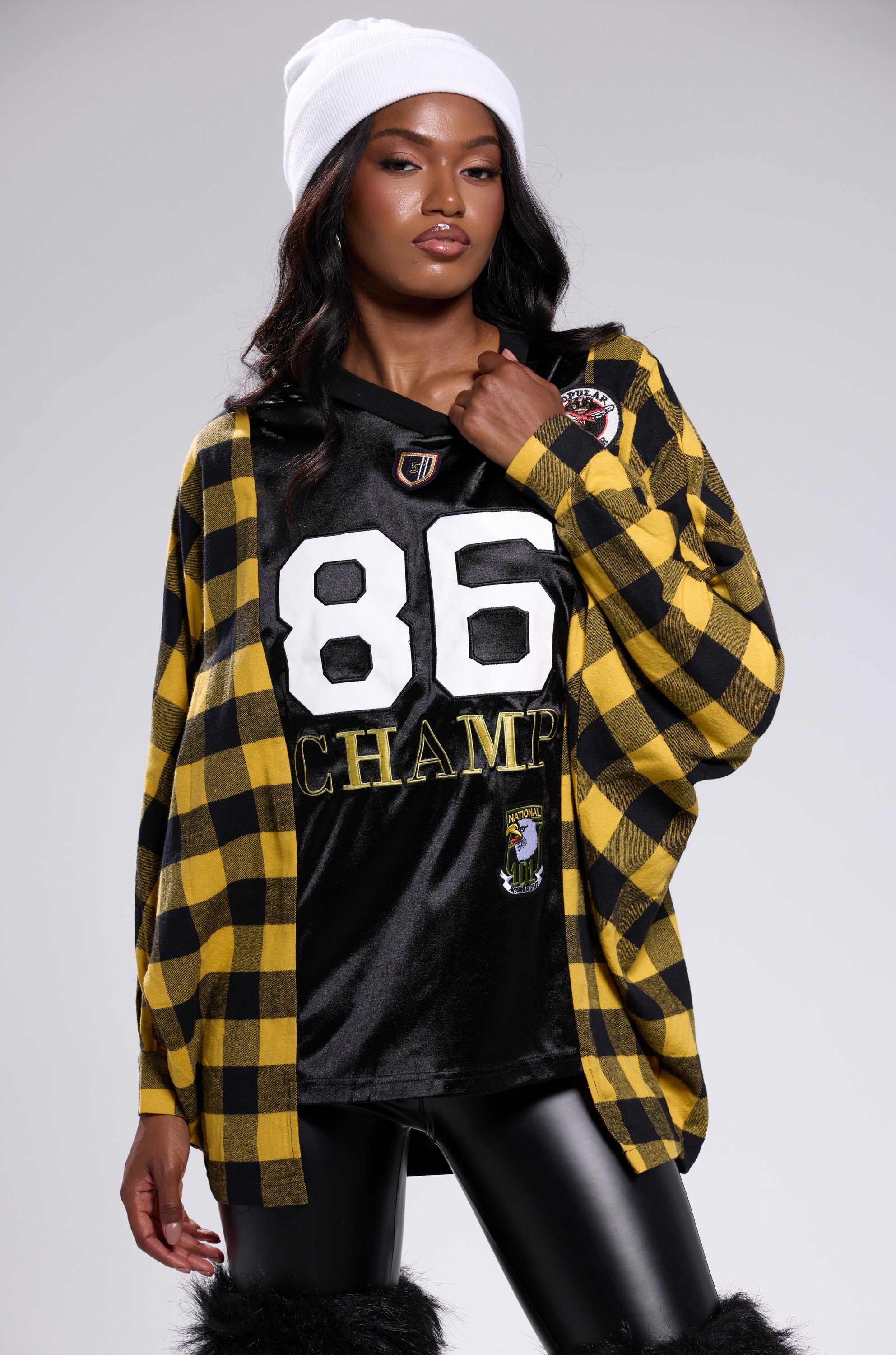 A woman poses confidently against a light gray background wearing a white beanie, black leather pants, and the NEW CHAMP REBUILT JERSEY FLANNEL TOP.