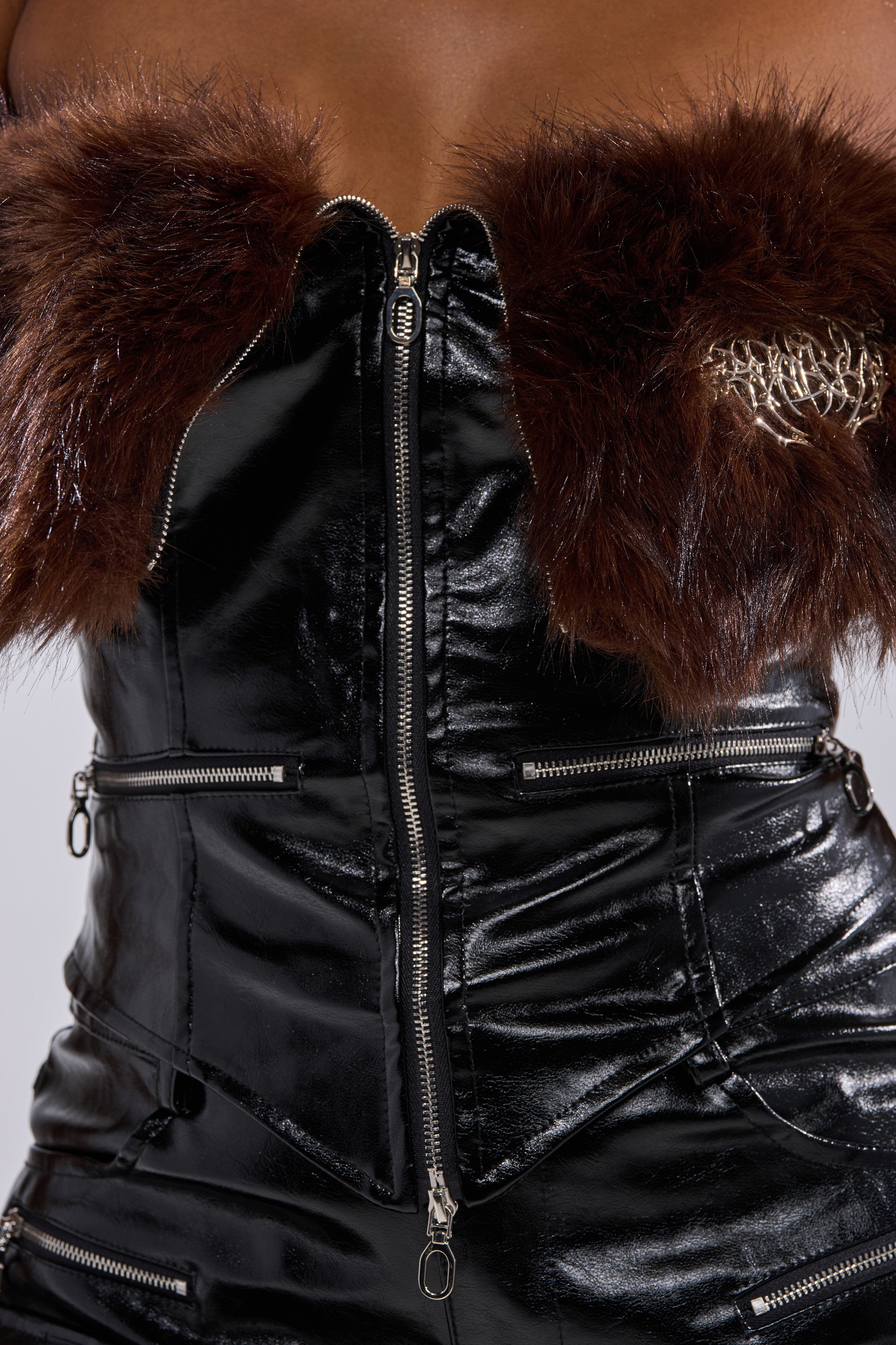 The ALL THE BIG ONES CORSET WITH FUR is a faux leather corset with a waist-defining silhouette, brown faux fur trim at the top, and metallic front zippers, shown against a neutral background.
