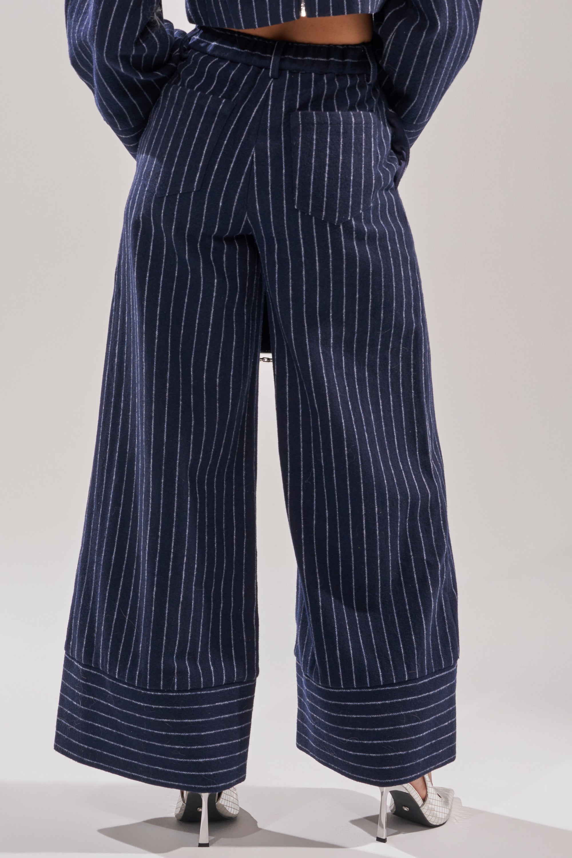 Someone wearing the STRICTLY BUSINESS PINSTRIPE TROUSER, featuring a wide-leg silhouette. 4