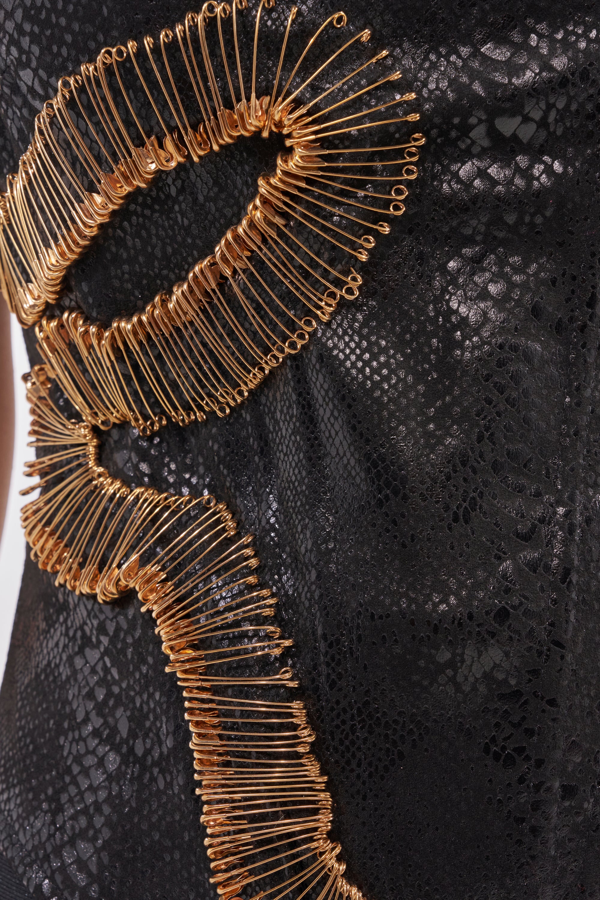 Close-up of the VENOMOUS EMBELLISHED PU CORSET—a black, shiny snakeskin-patterned top with swirling gold safety pin accents arranged in an artistic curve. 8