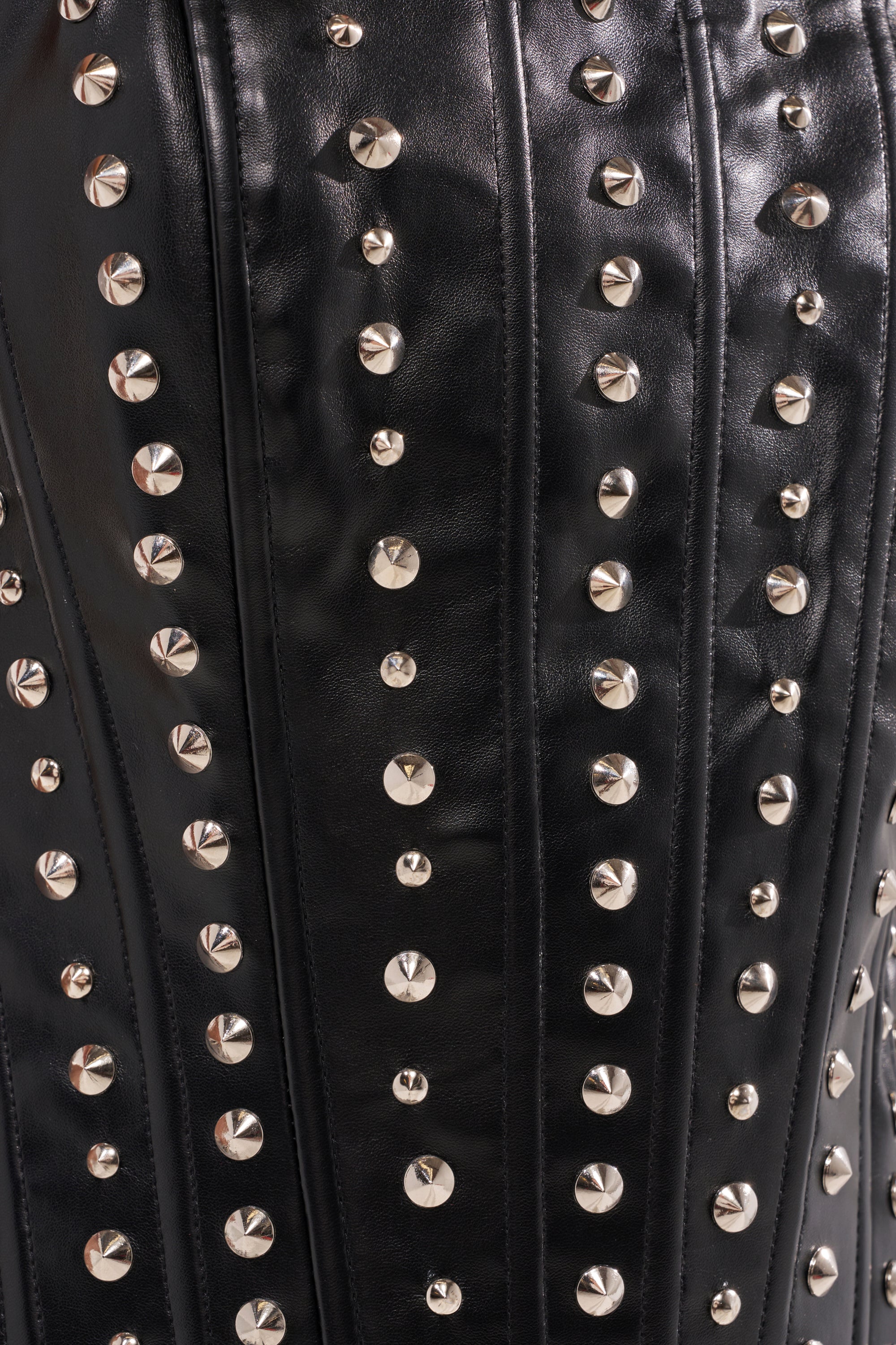 Close-up of the DONT HUG ME FAUX LEATHER CORSET, featuring black faux leather fabric with vertical stitching and rows of round silver metal studs.