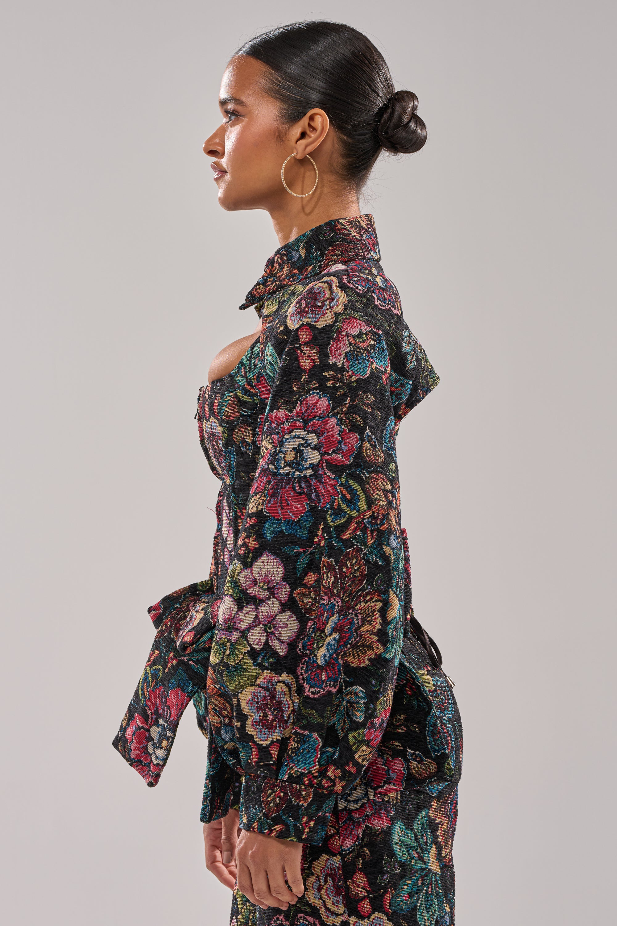 A woman with slicked-back hair in a bun wears large hoop earrings and the PRETTY LADY BROCADE BOLERO, posing in profile against a plain, light gray background. 3