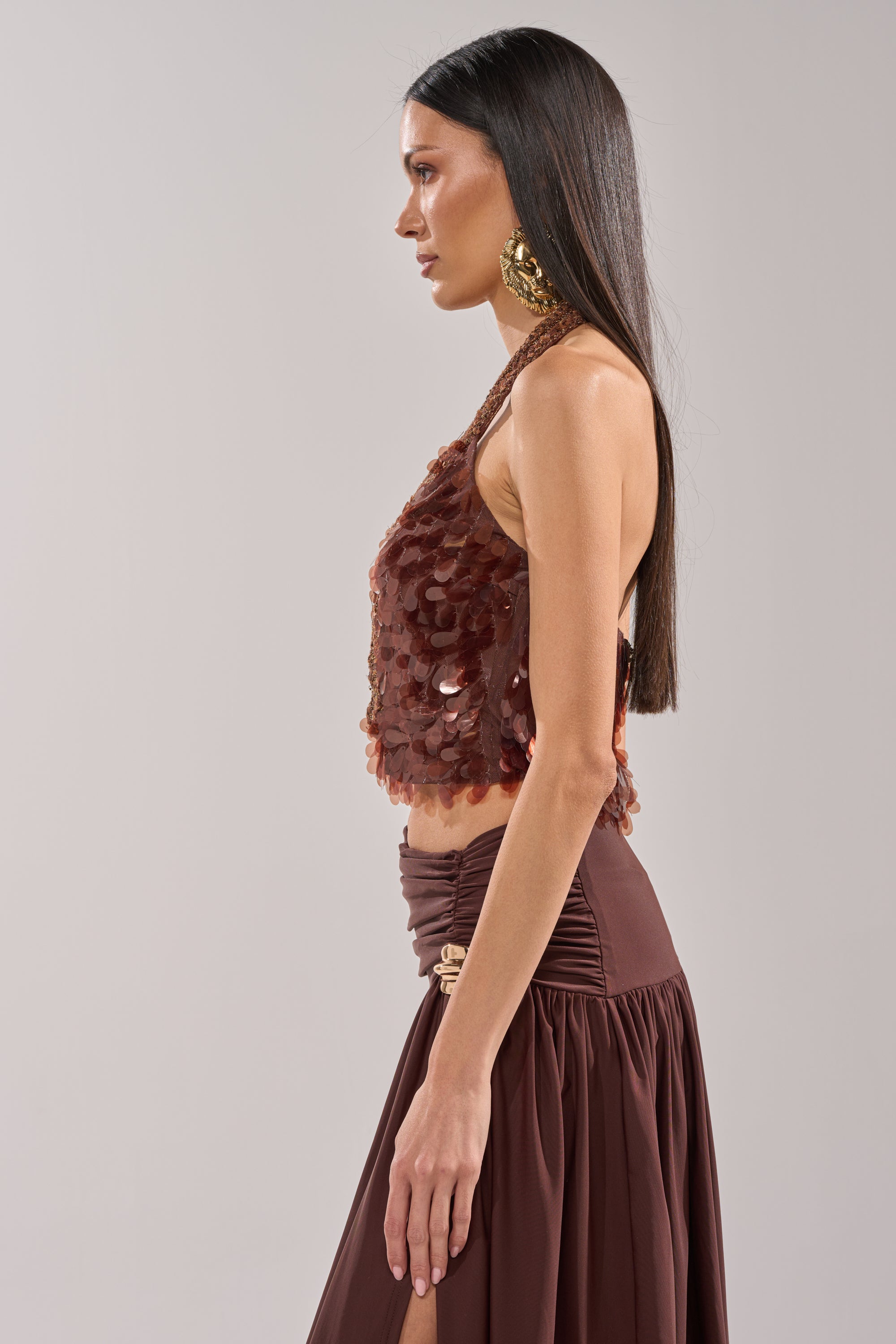 A woman with long straight hair poses in profile against a light background, wearing the ISLAND GIRL SEQUIN BLOUSE and matching skirt, styled with large gold earrings for a chic party look. 2