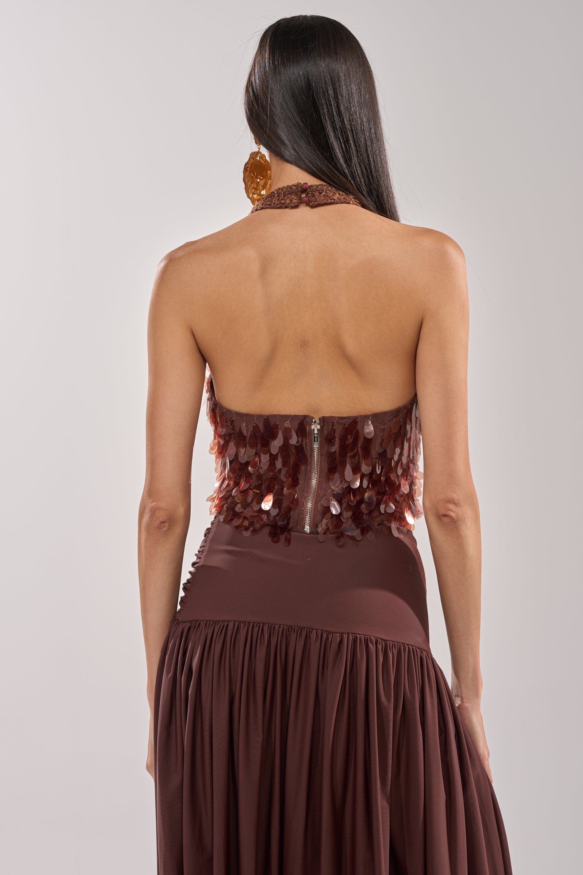 A woman with long dark hair is seen from behind wearing the ISLAND GIRL SEQUIN BLOUSE, a brown strapless top featuring a bronze sequin bodice, set against a plain background. 3