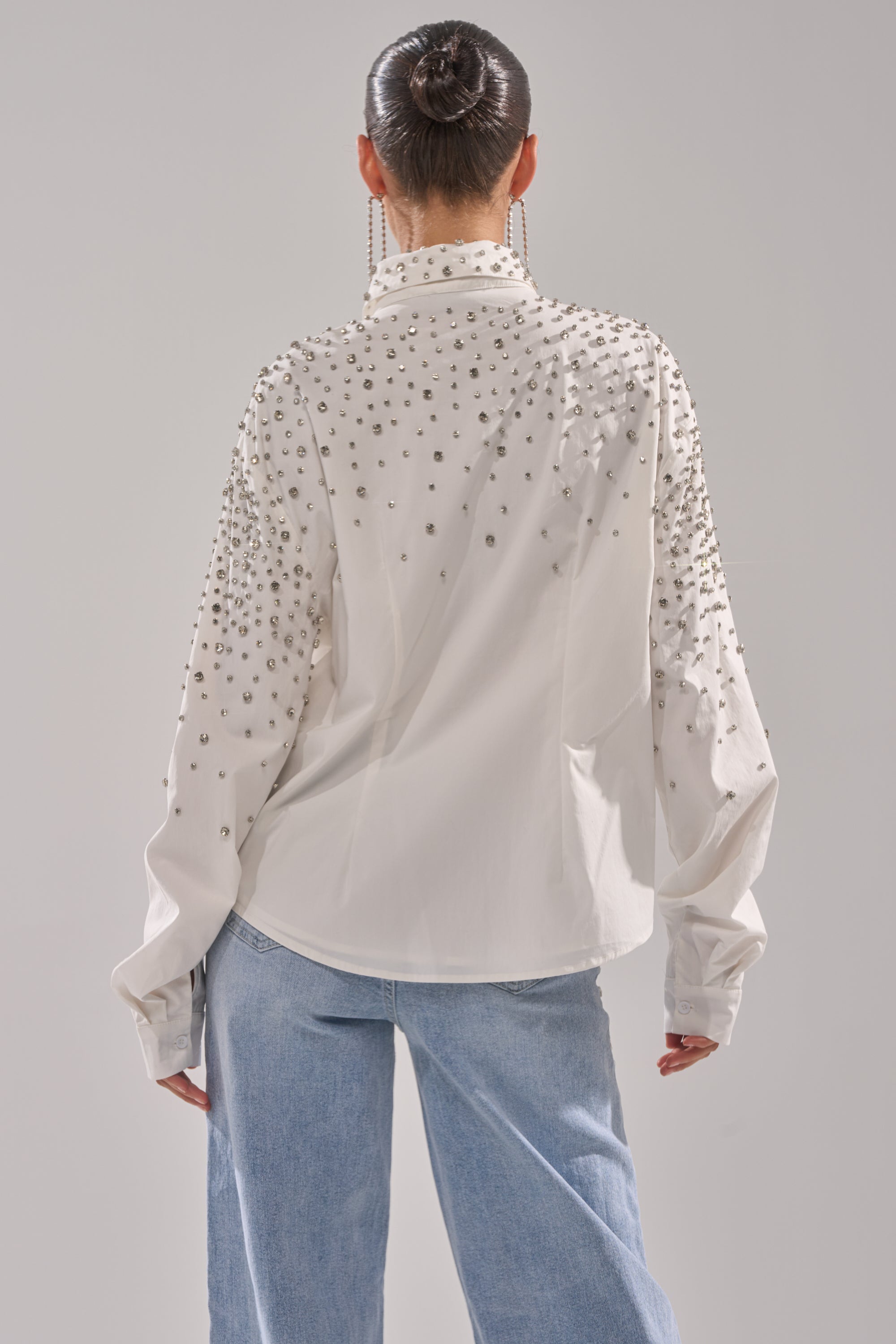 A person with dark hair in a bun, shown from the back against a plain background, wears the DIAMONDS FOREVER BUTTON DOWN with rhinestone embellishments and loose blue jeans.