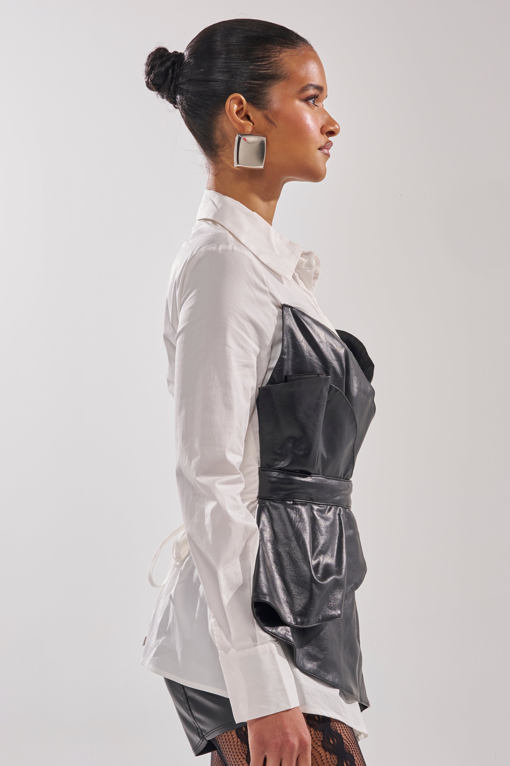 A woman with slicked-back hair in a bun, wearing large square earrings and the IS THIS CRAZY ENOUGH BLOUSE, stands in profile against a plain light background. 4