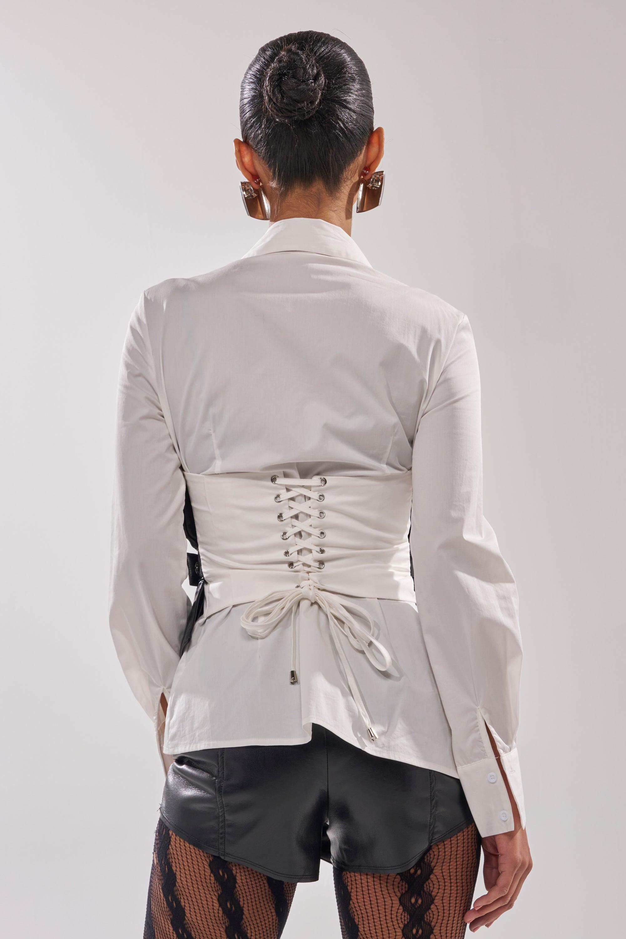 A person with hair in a sleek bun wears the IS THIS CRAZY ENOUGH BLOUSE styled over black leather shorts and patterned black tights, facing away from the camera against a plain background. 5