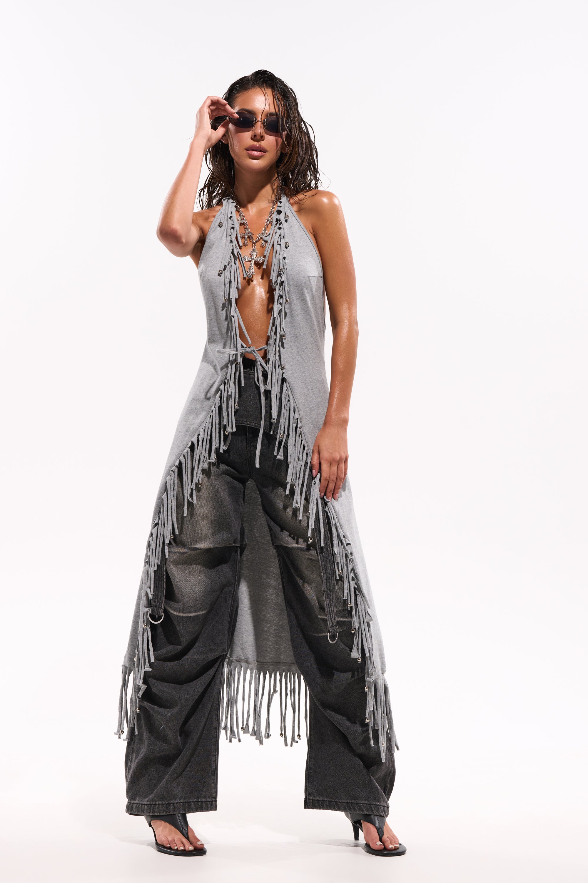 A woman poses confidently in the FRINGE GIRL BLOUSE with a deep neckline, sunglasses, black wide-leg jeans, and black heels against a plain white background. 0