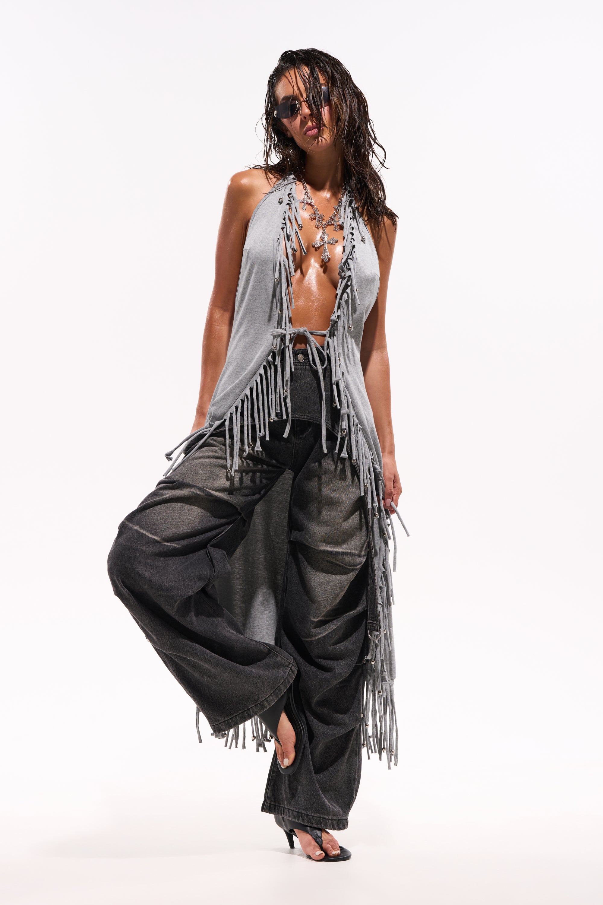 A person poses confidently against a plain white background wearing the FRINGE GIRL BLOUSE, sunglasses, loose-fitting dark jeans, and black high-heeled sandals. 1