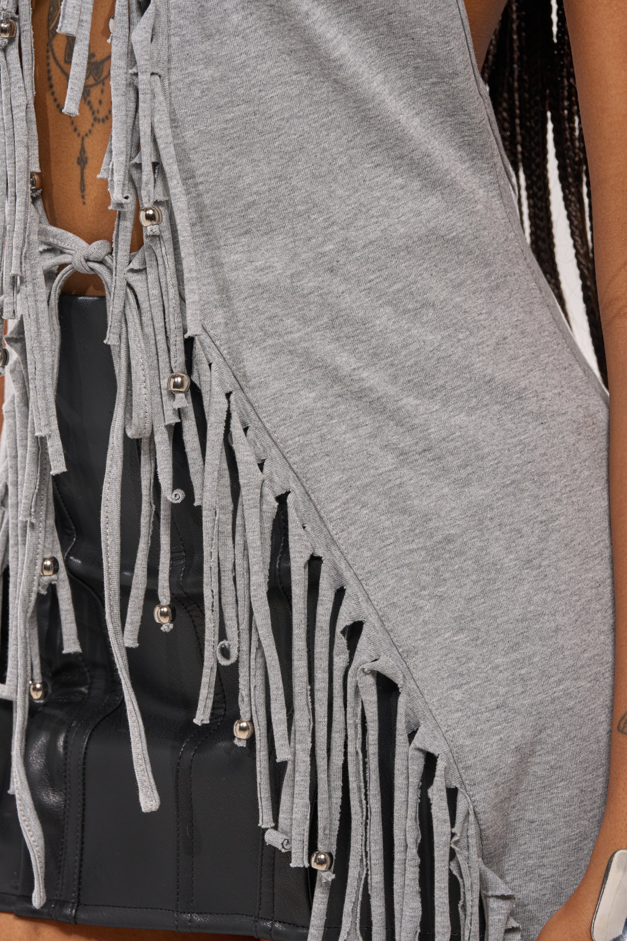 Close-up of a person wearing the FRINGE GIRL BLOUSE, a statement sleeveless top with metal beads, paired with a black leather skirt. Visible tattoo and braided hair add to the edgy, modern vibe inspired by boho fringe halter styles. 8