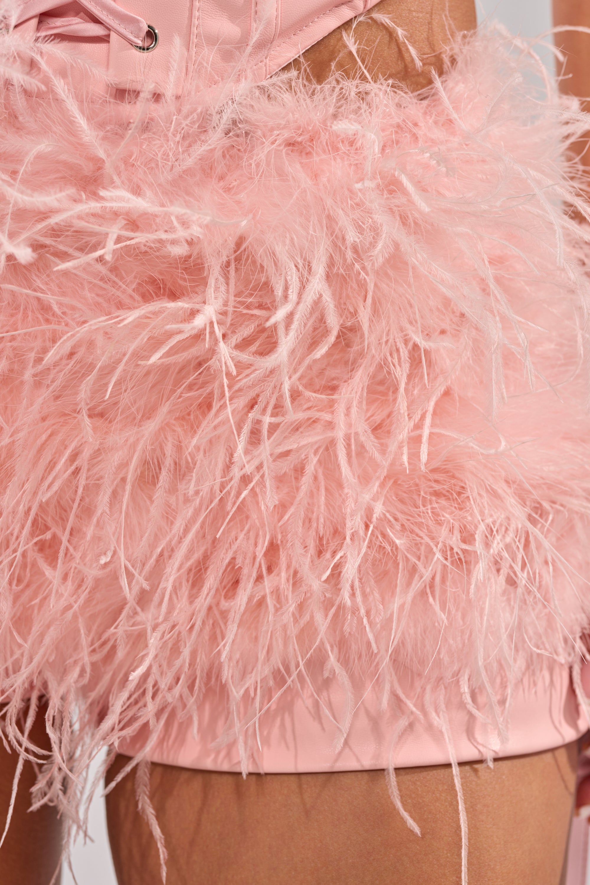 Close-up of a person wearing the STAR OF THE NIGHT FUR SHORT, a light pink satin outfit with feather detailing, creating a textured and stylish appearance. 12