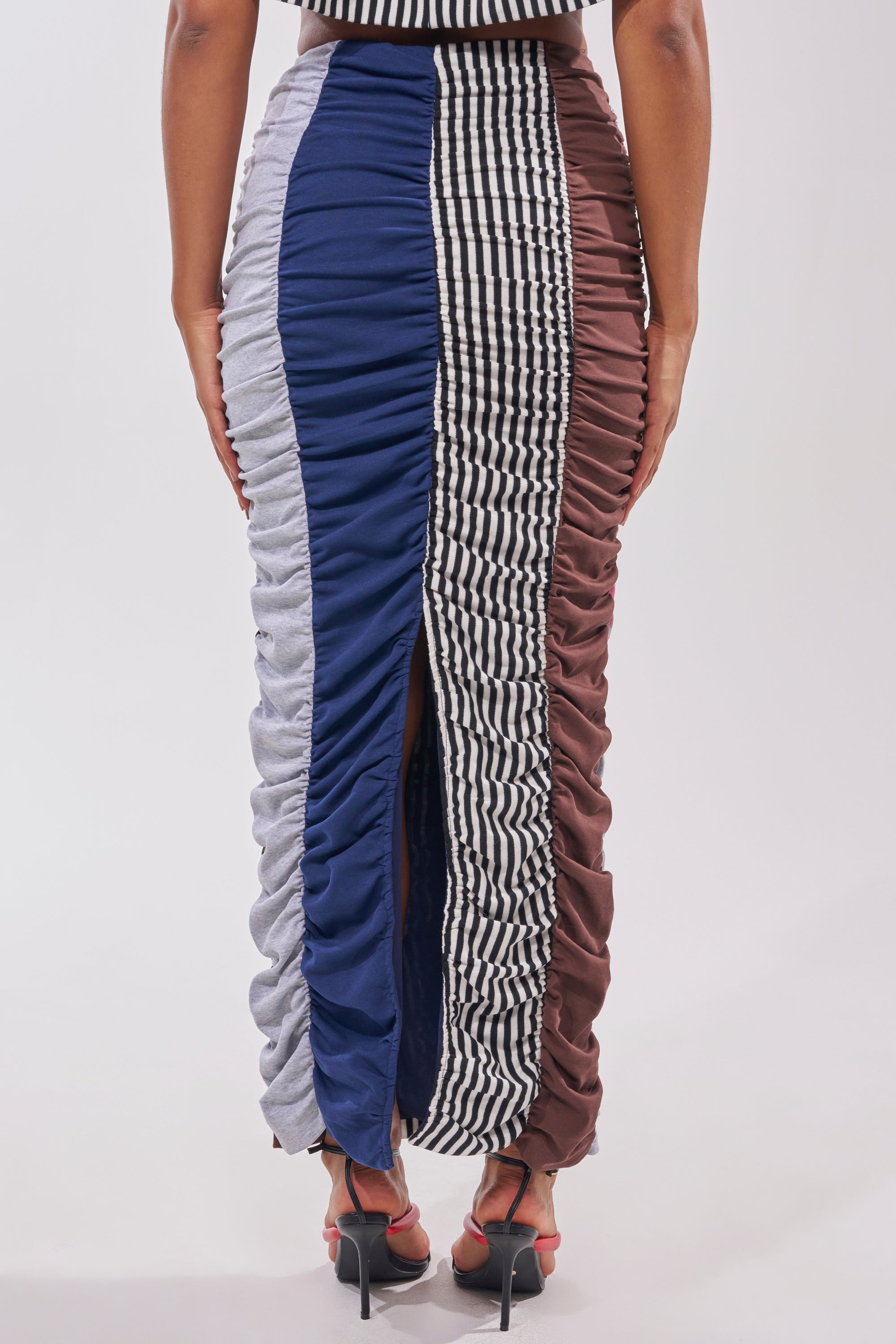 Wearing the THAT GIRL GRAPHIC TEE MAXI SKIRT—a long, patchwork-inspired skirt with vertical blue, gray, brown, and black-and-white checkered panels and a back slit—styled with heels. 4