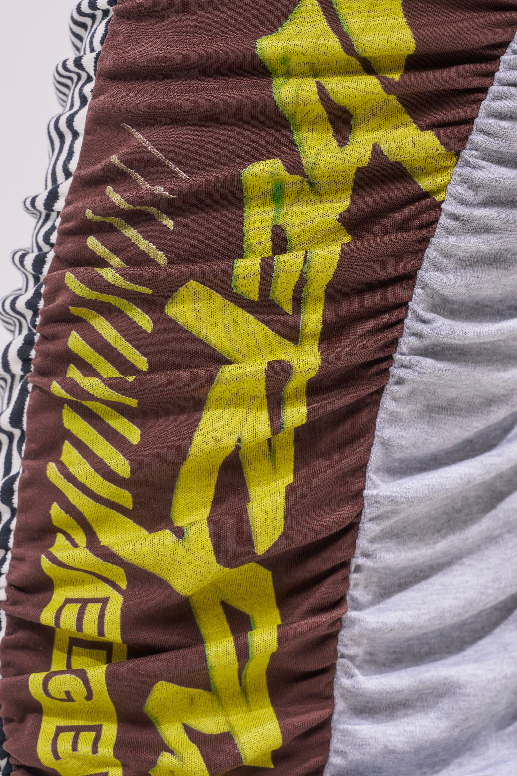 Close-up of ruched brown and gray fabric from the THAT GIRL GRAPHIC TEE MAXI SKIRT, featuring bold yellow text and black-and-white striped trim along the left edge for a graphic tee-inspired look. 6
