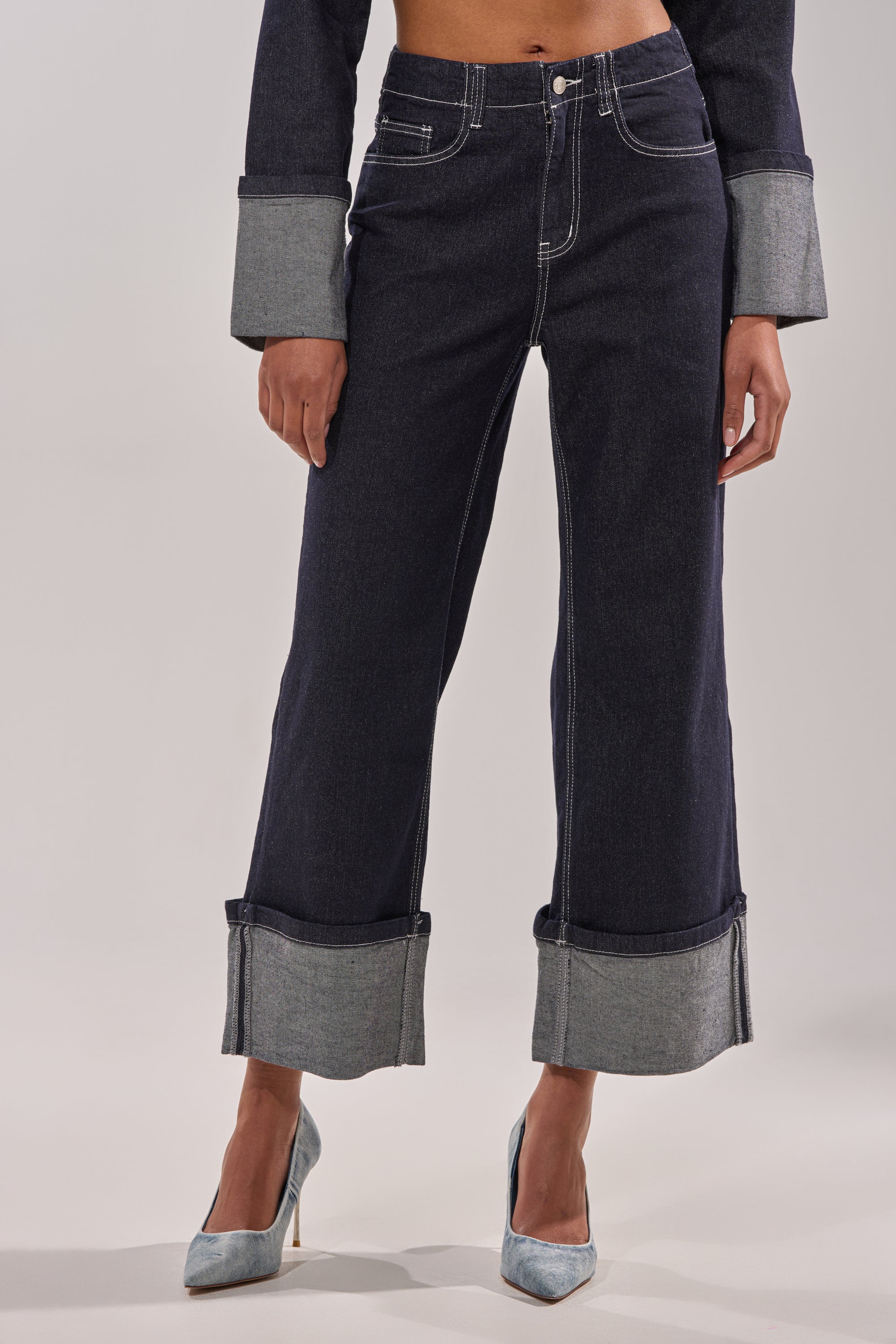 A person sports the DON'T TALK TO ME WIDE LEG DENIM JEANS—with a high-rise, wide-leg fit and large cuffs—paired with a matching denim jacket and light blue heels, set against a plain, light background. 1