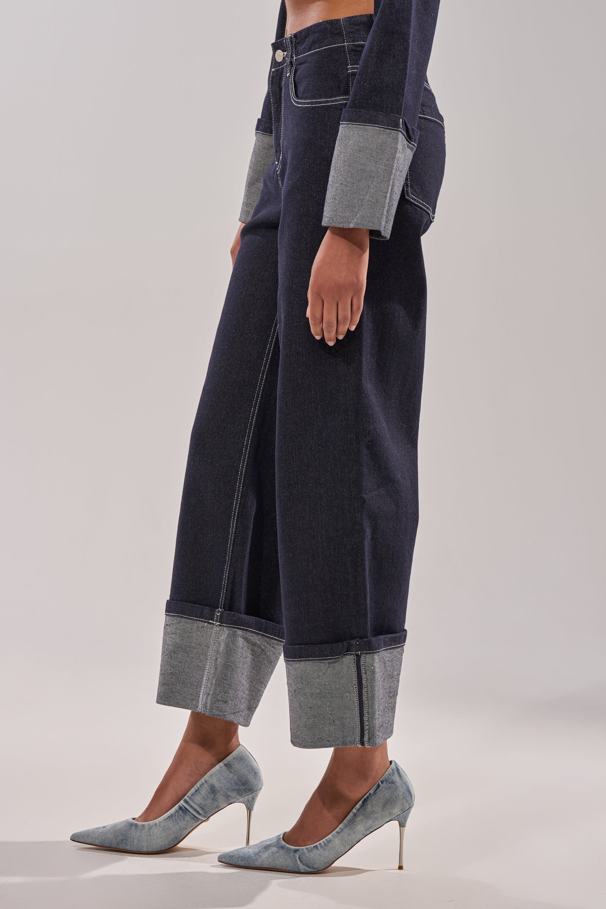 A person models the DON'T TALK TO ME WIDE LEG DENIM JEANS, showcasing their dark-wash, wide-leg, high-rise style with a cuffed hem. Paired with light blue high heels, only the lower half is visible against a plain light background. 4