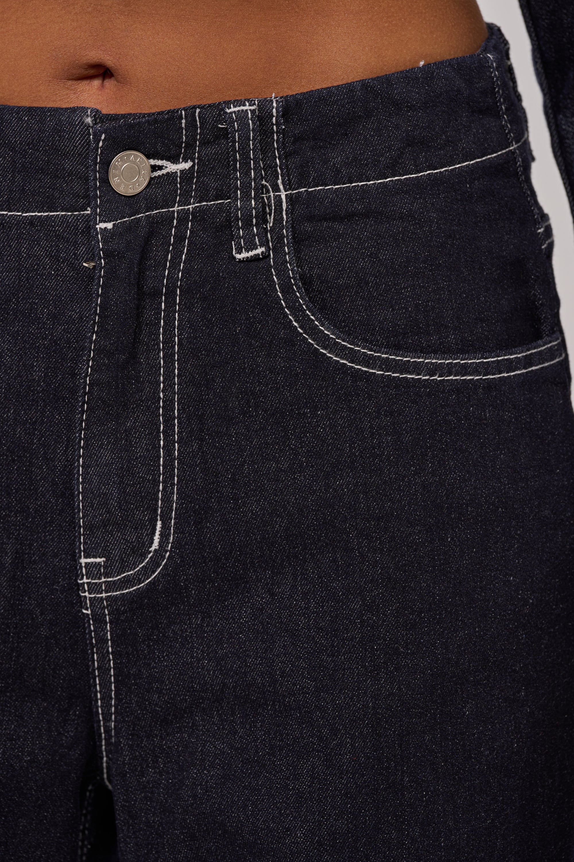 Close-up of a person wearing the DON'T TALK TO ME WIDE LEG DENIM JEANS in dark-wash denim with white stitching, front button, zipper fly, partial waistband, and pockets visible. 7