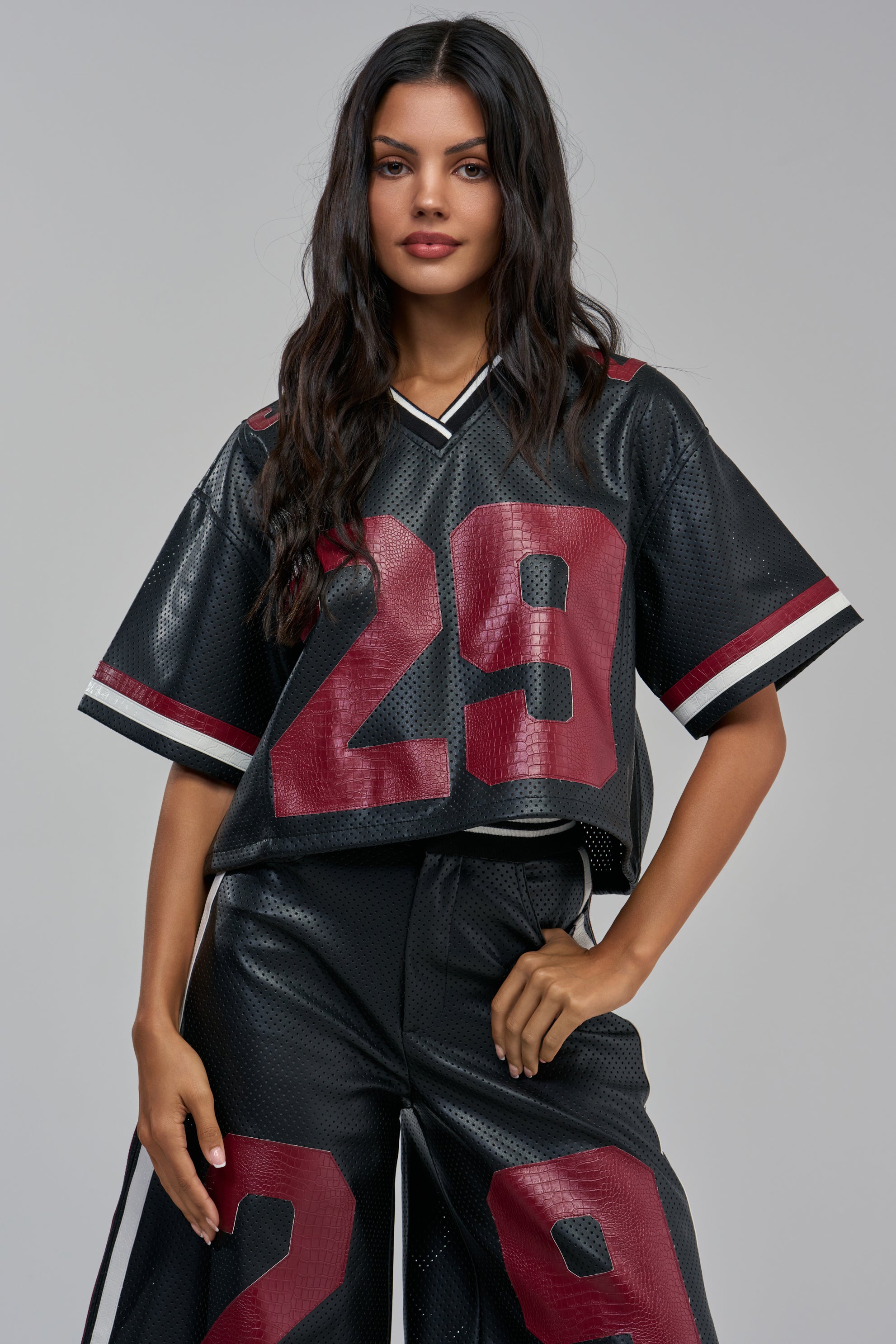 A person wearing a LUCKY 29 JERSEY IN BLACK MULTI, consisting of a cropped faux leather jersey and matching shorts, both featuring a large maroon number 29 and white and maroon striped trim.