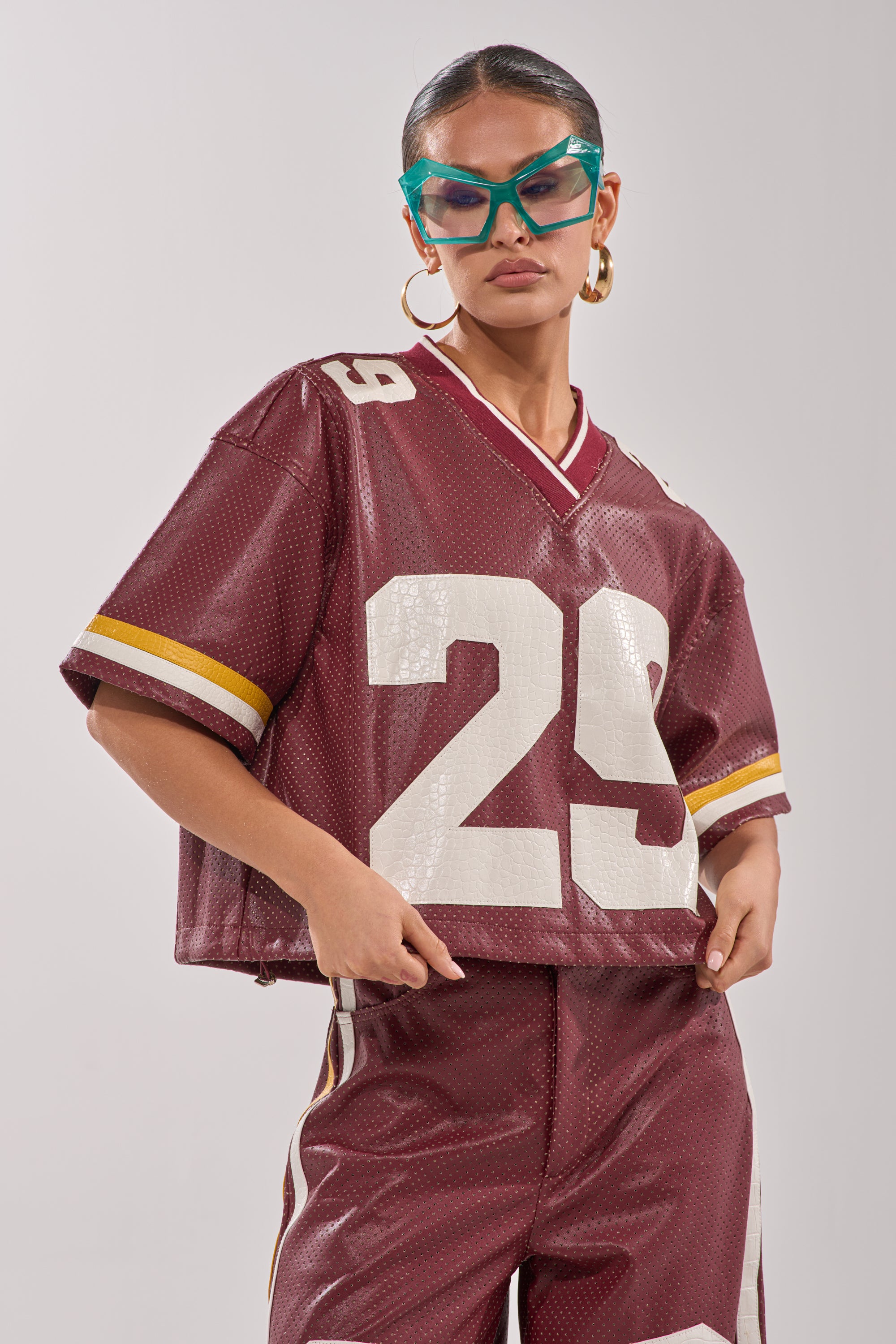 A person poses confidently against a neutral background, wearing teal sunglasses, gold hoop earrings, and the maroon LUCKY 29 JERSEY with varsity-style numbers, paired with matching pants. 1