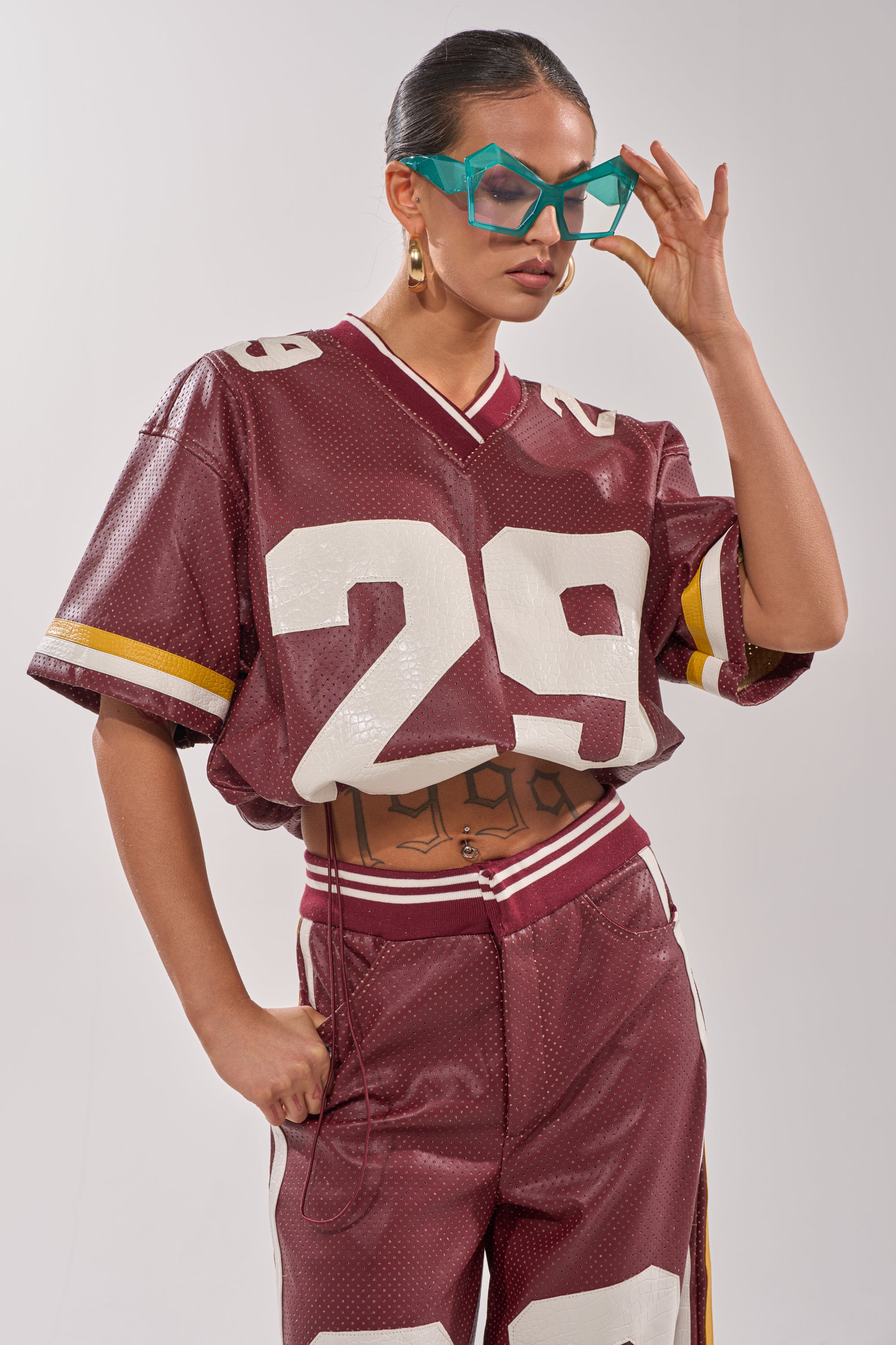 A person poses confidently in the LUCKY 29 JERSEY, matching pants, large turquoise glasses, and gold hoop earrings, with one hand adjusting their glasses. 2