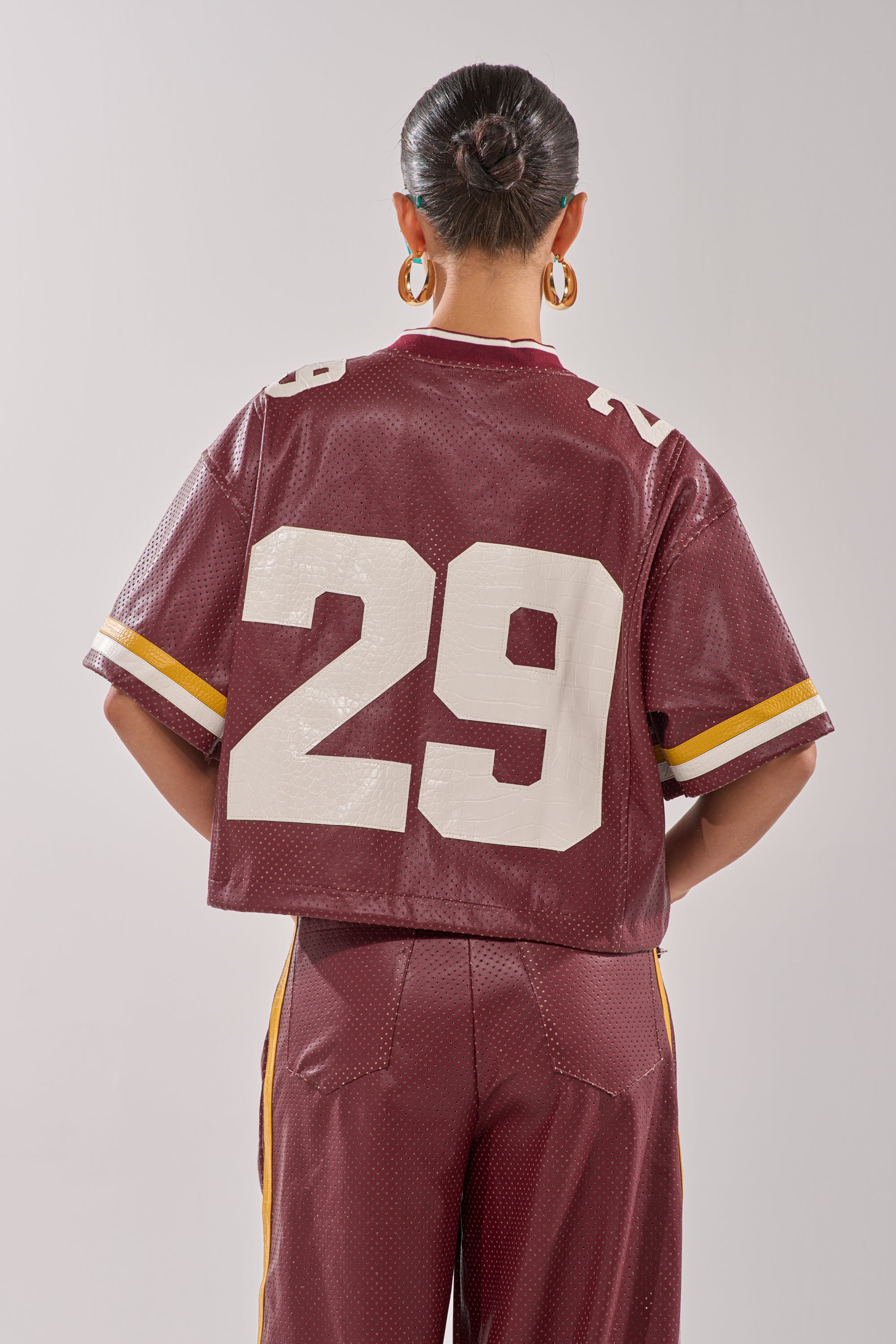 A person with dark hair in a bun and hoop earrings stands facing away, wearing the burgundy LUCKY 29 JERSEY with the number 29 on the back, paired with matching maroon pants. 6