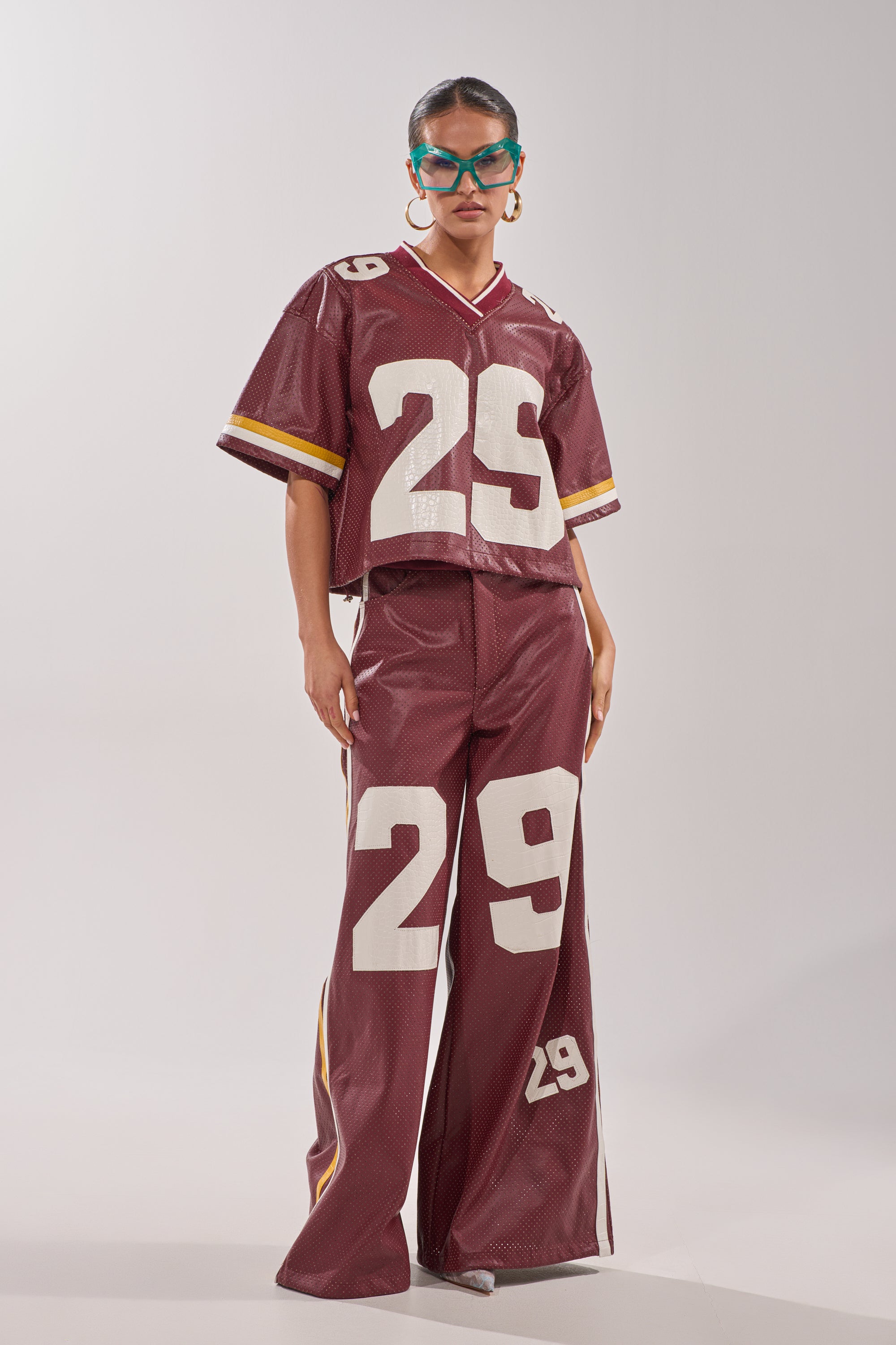 Wearing the LUCKY 29 JERSEY in burgundy with white "29" on both the top and pants, plus large hoop earrings and blue sunglasses, this person stands against a plain light background. 8