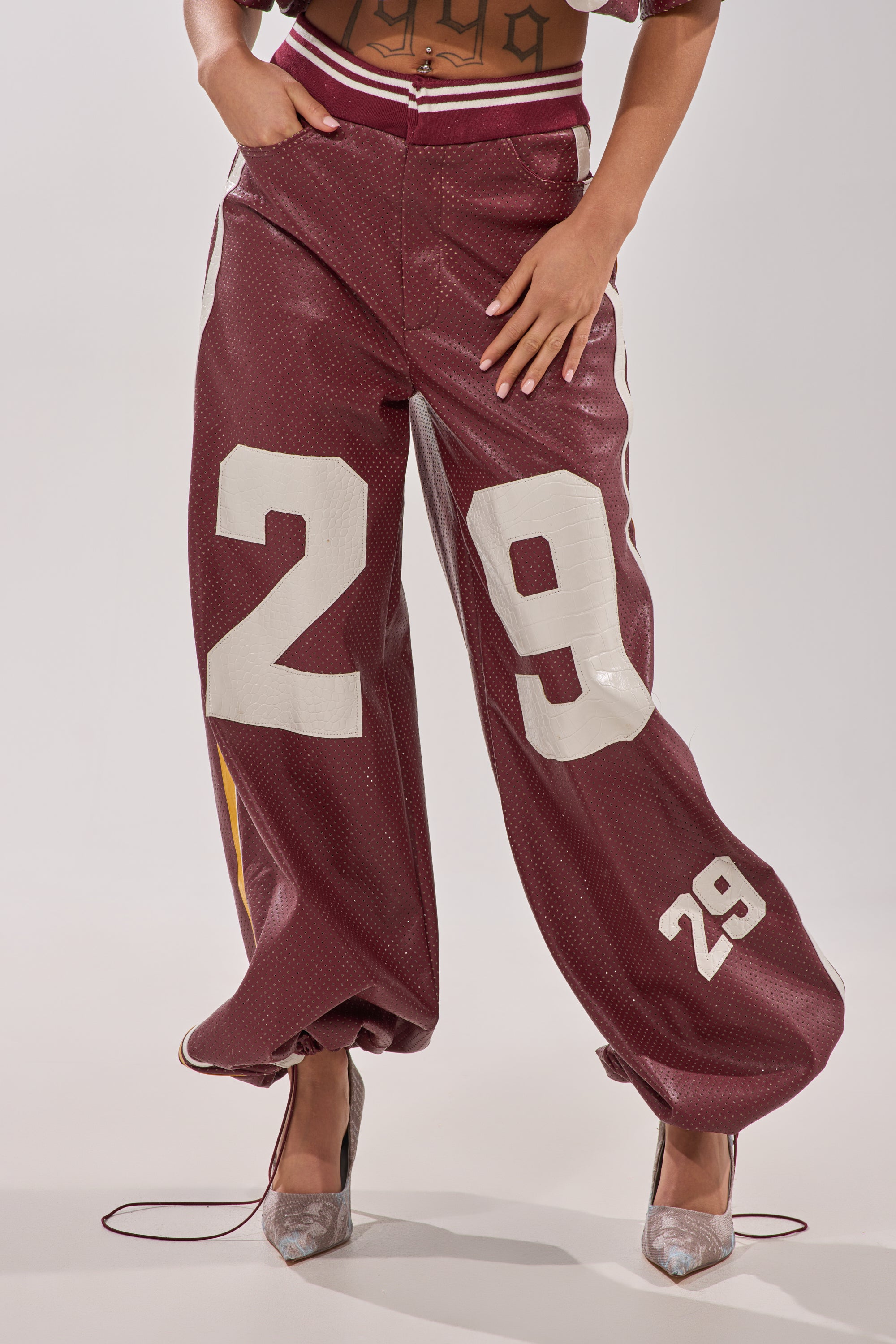A person wears the LUCKY 29 TROUSER—burgundy wide-leg pants featuring large white "29" prints on each leg—paired with high heels against a plain, light background. 4