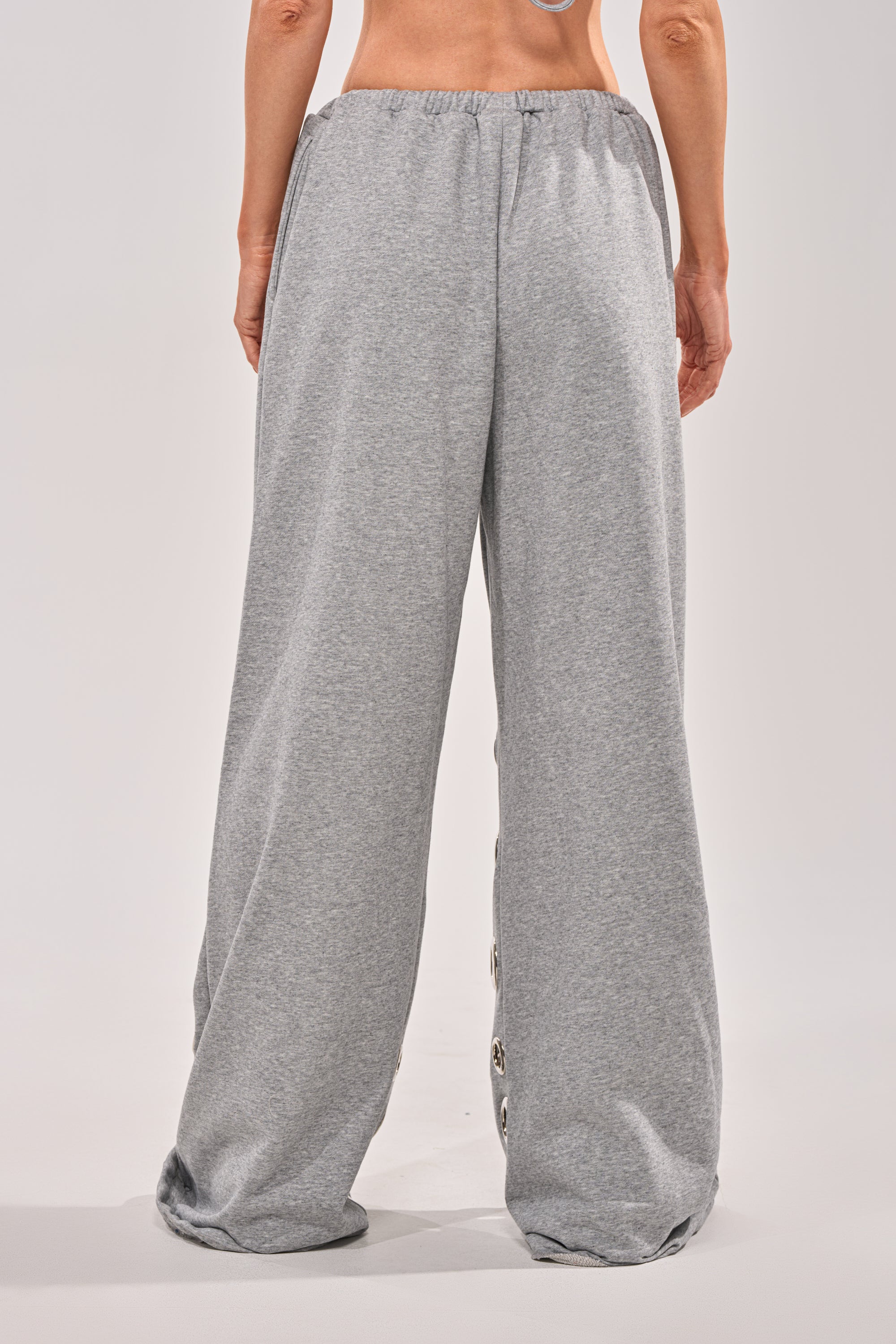 A person is shown from the waist down wearing the CHECK IT OUT GROMMET JOGGER, featuring grey wide-leg sweats with an elastic waistband, standing against a neutral background. 4