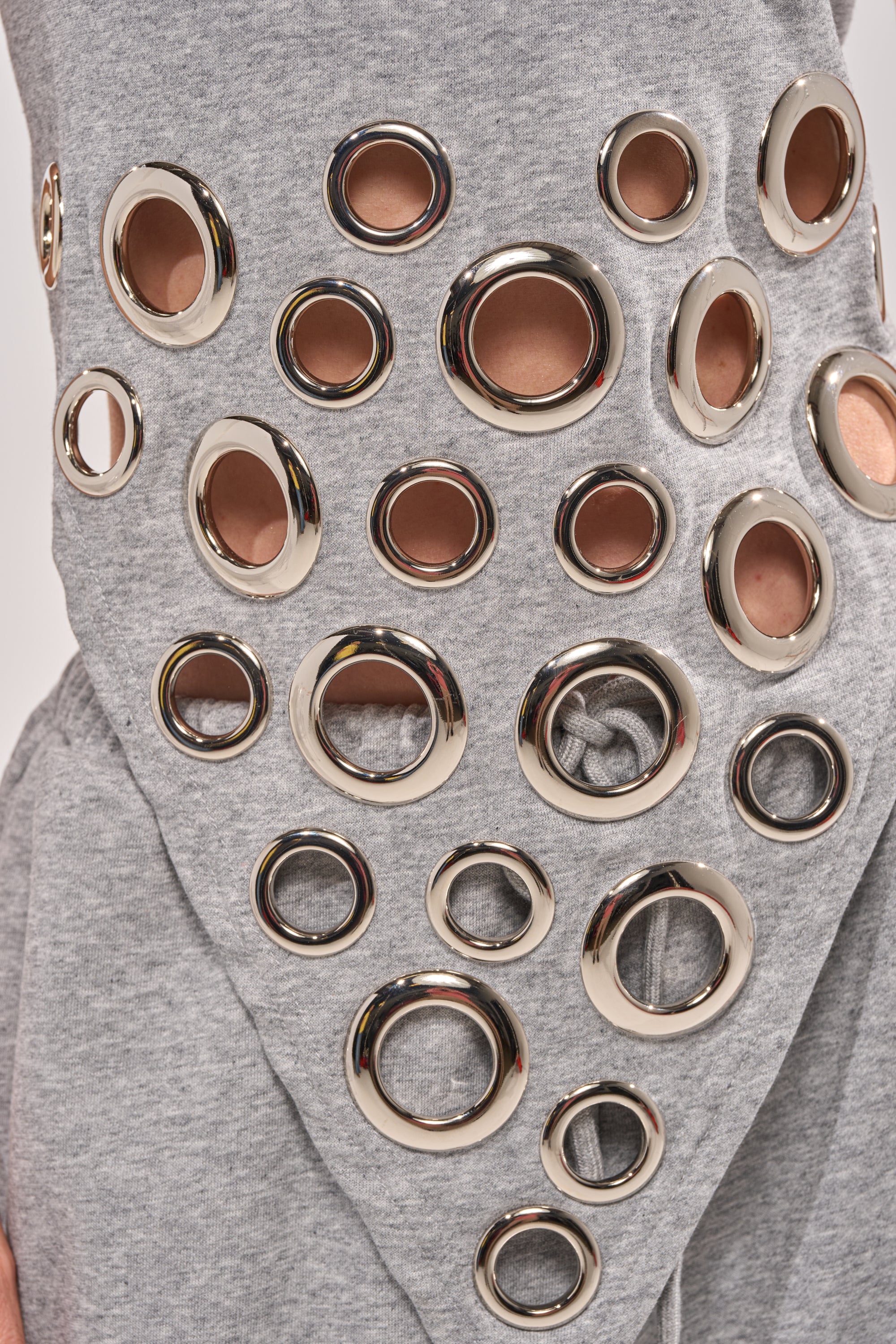 Close-up of the CHECK IT OUT GROMMET TOP in gray, featuring metallic circular grommets in assorted sizes that reveal skin for a bold streetwear style. 8