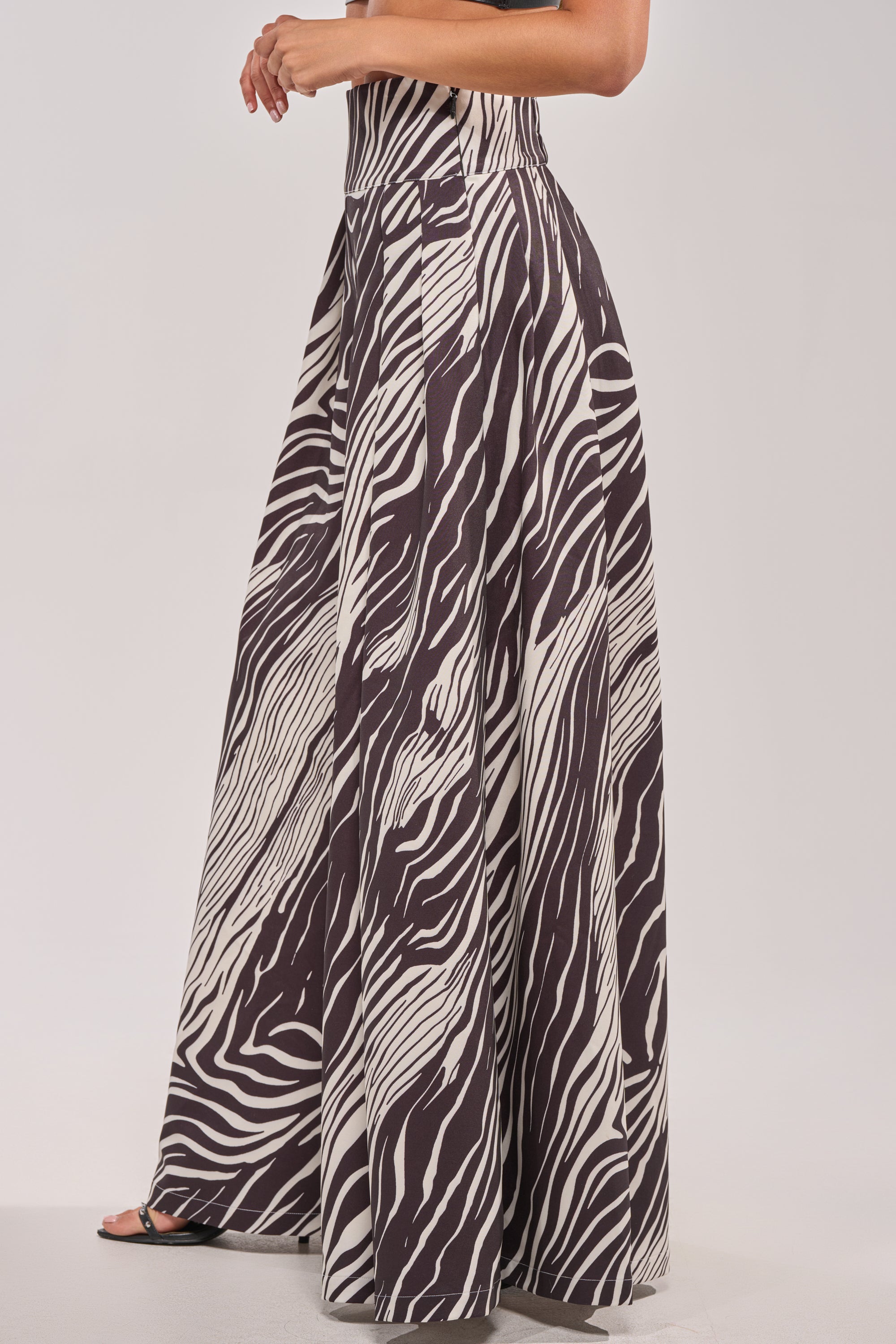 A person stands sideways in the WILD AND FREE ZEBRA TROUSER, featuring a high rise and wide-leg silhouette. The flowy pants are styled with open-toe shoes against a plain, light background.