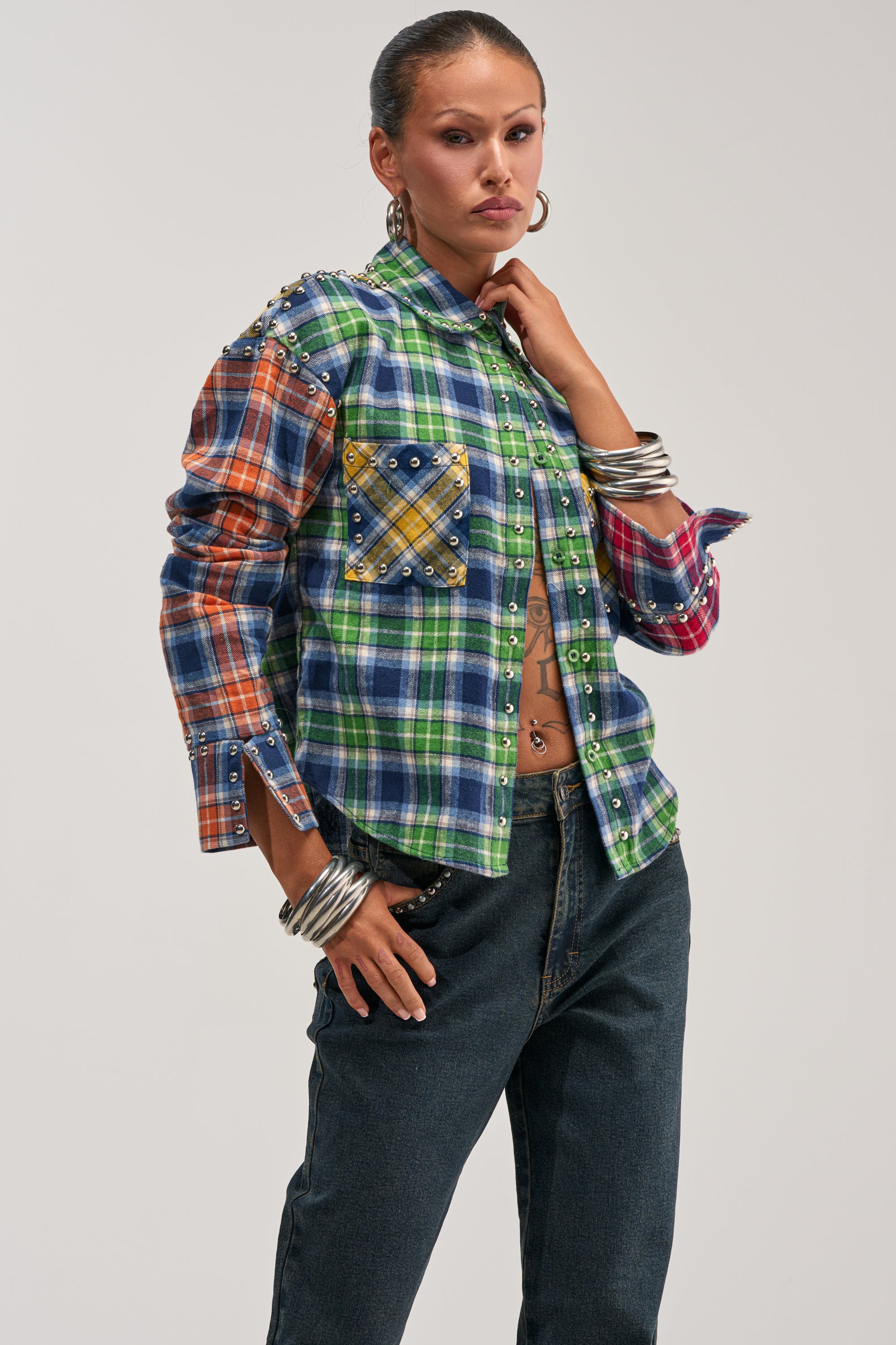 Wearing the JUST FOR FUN PLAID EMBELLISHED BUTTON DOWN, styled with large hoop earrings, silver bangles, and dark jeans, this person poses confidently against a plain light background for a bold streetstyle look.