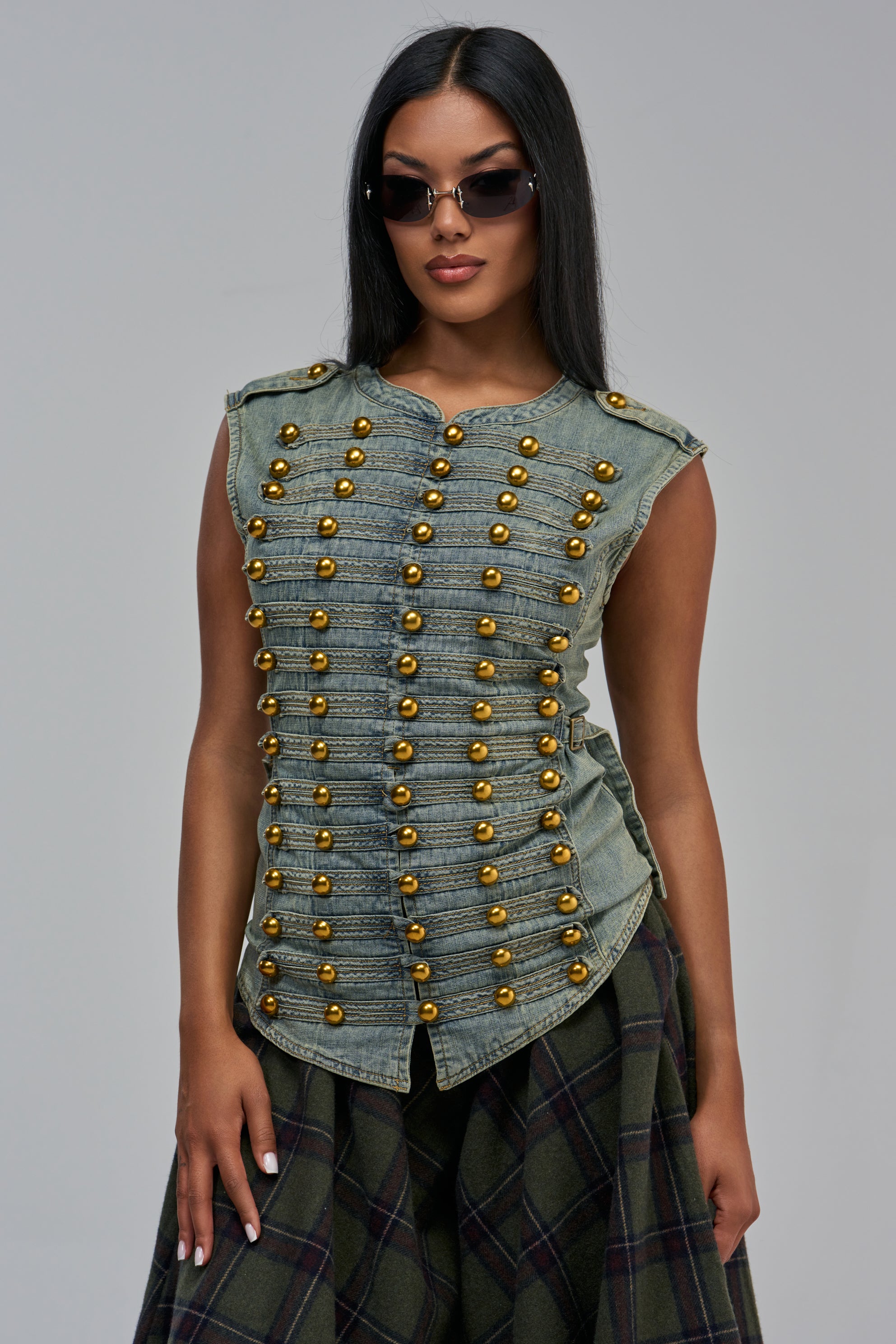 ON TOP DENIM TOP, a sleeveless light-wash denim top with rows of gold-toned spherical buttons, worn with a dark plaid skirt for a military-inspired streetwear look.