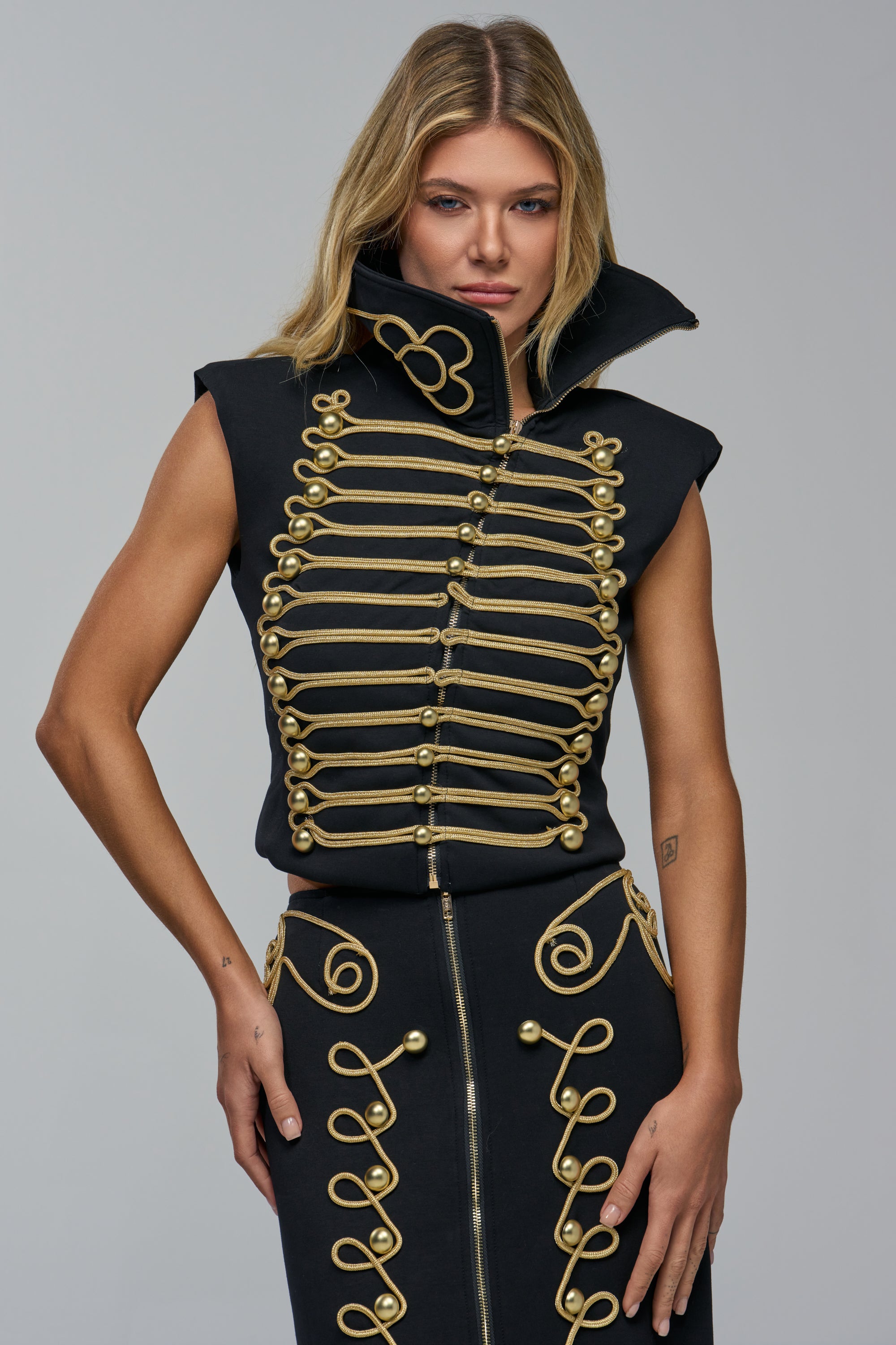 The RARE BREED SCUBA TOP is a sleeveless black military-inspired scuba top with a high collar and decorative gold cord trim featuring spherical buttons.