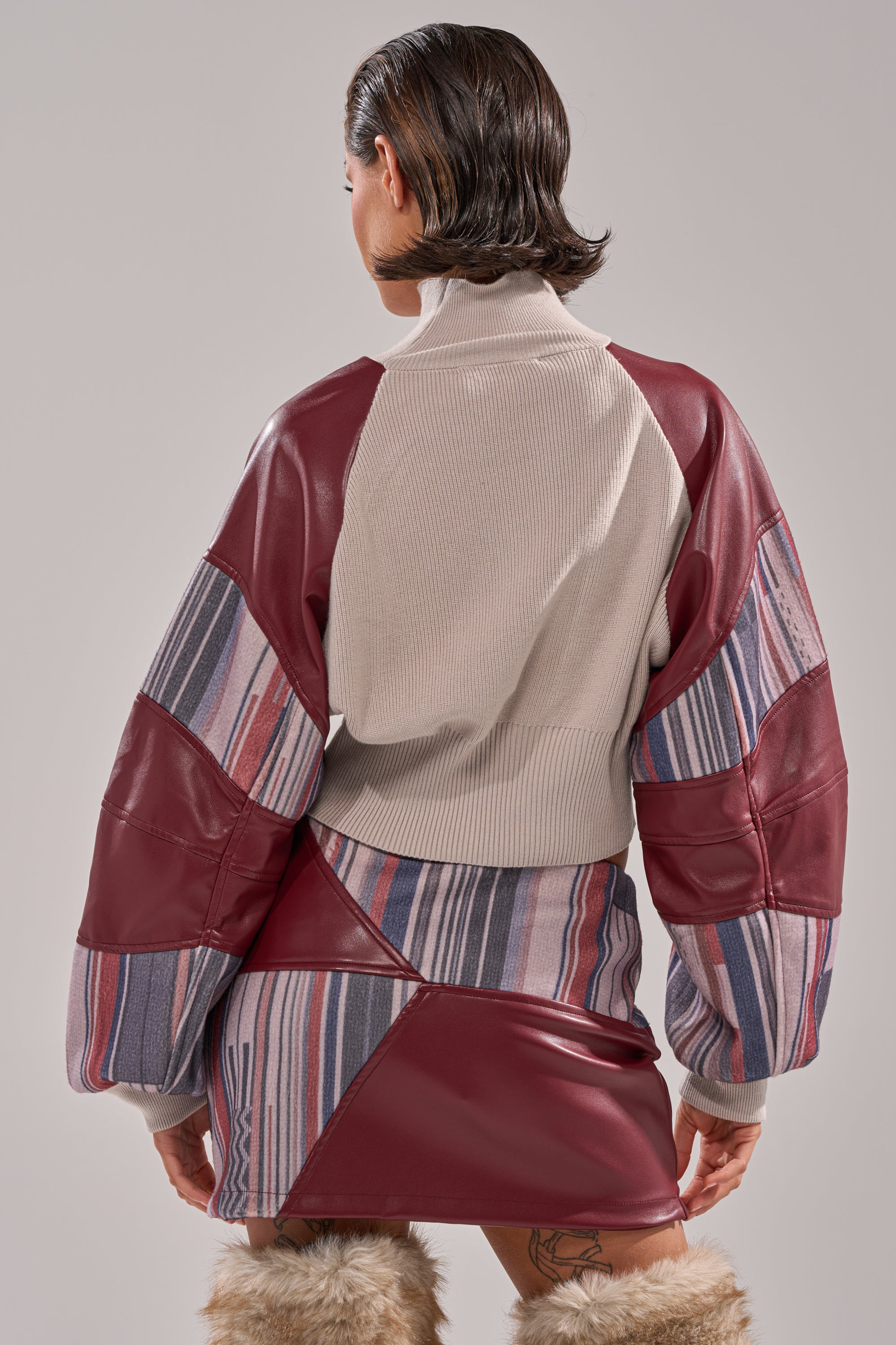 A person with short, slicked-back hair is seen from behind in the FEELING THE VIBES CROPPED GREY SWEATER. They pair it with a matching skirt and furry boots against a plain light gray background. 3