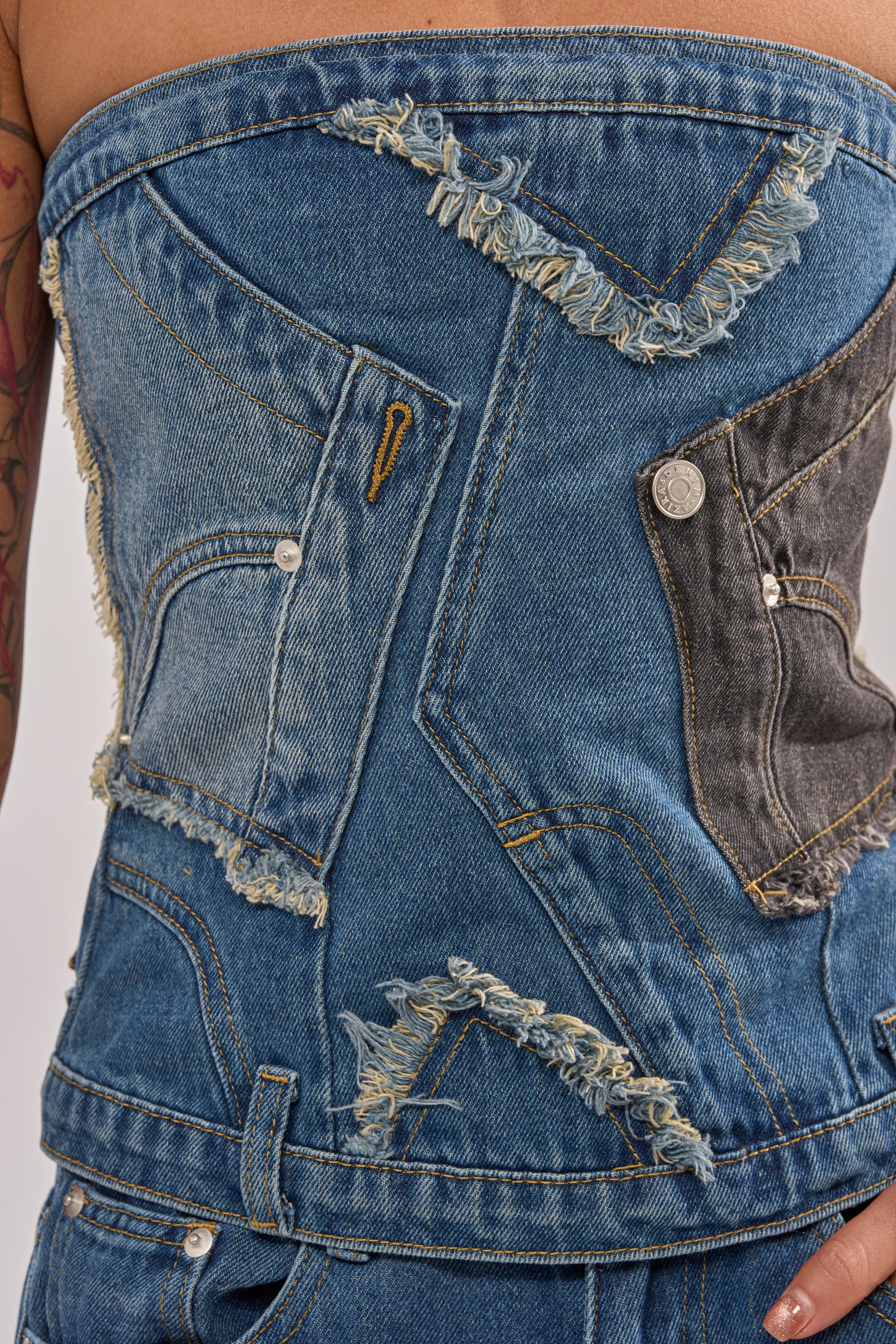 A close-up of a street style look showcases the MIXED MATCH DENIM CORSET, a strapless top featuring patchwork denim and frayed edges. A tattooed arm is partially visible on the left. 6