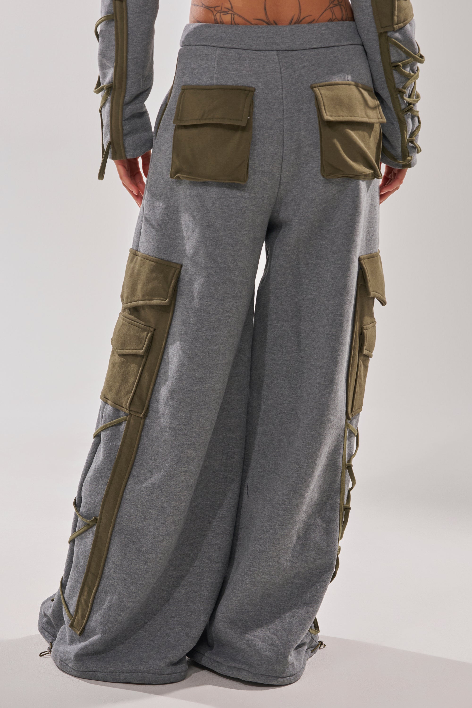 Someone is photographed from the back wearing the CRAZY IN LOVE TROUSER—high waisted, wide-leg cargo pants in olive green with multiple large pockets and lace-up side details.