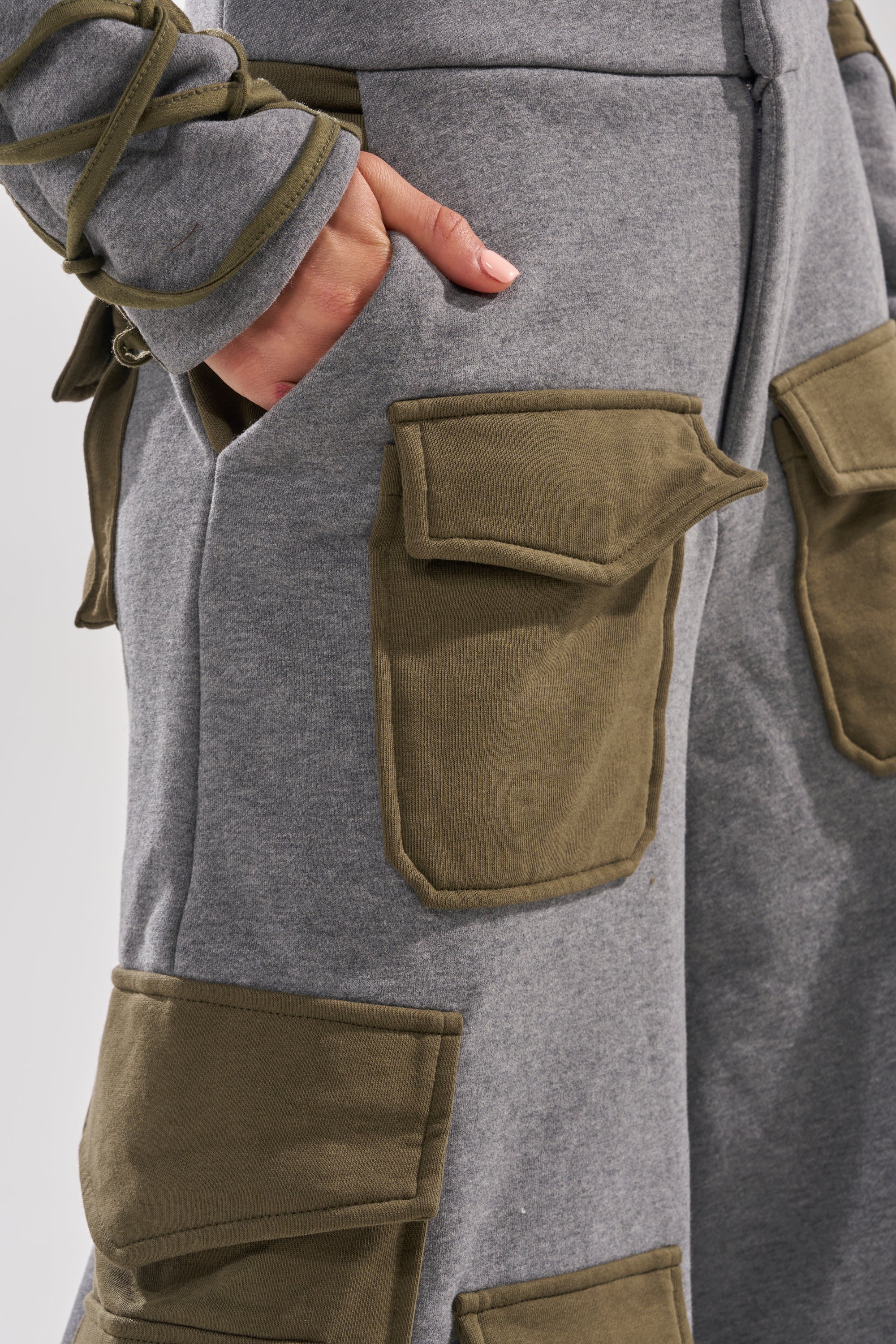 A close-up of a person wearing the CRAZY IN LOVE TROUSER, featuring high waist and large olive-green cargo pockets, their hand tucked in, highlighting a utilitarian fashion vibe.