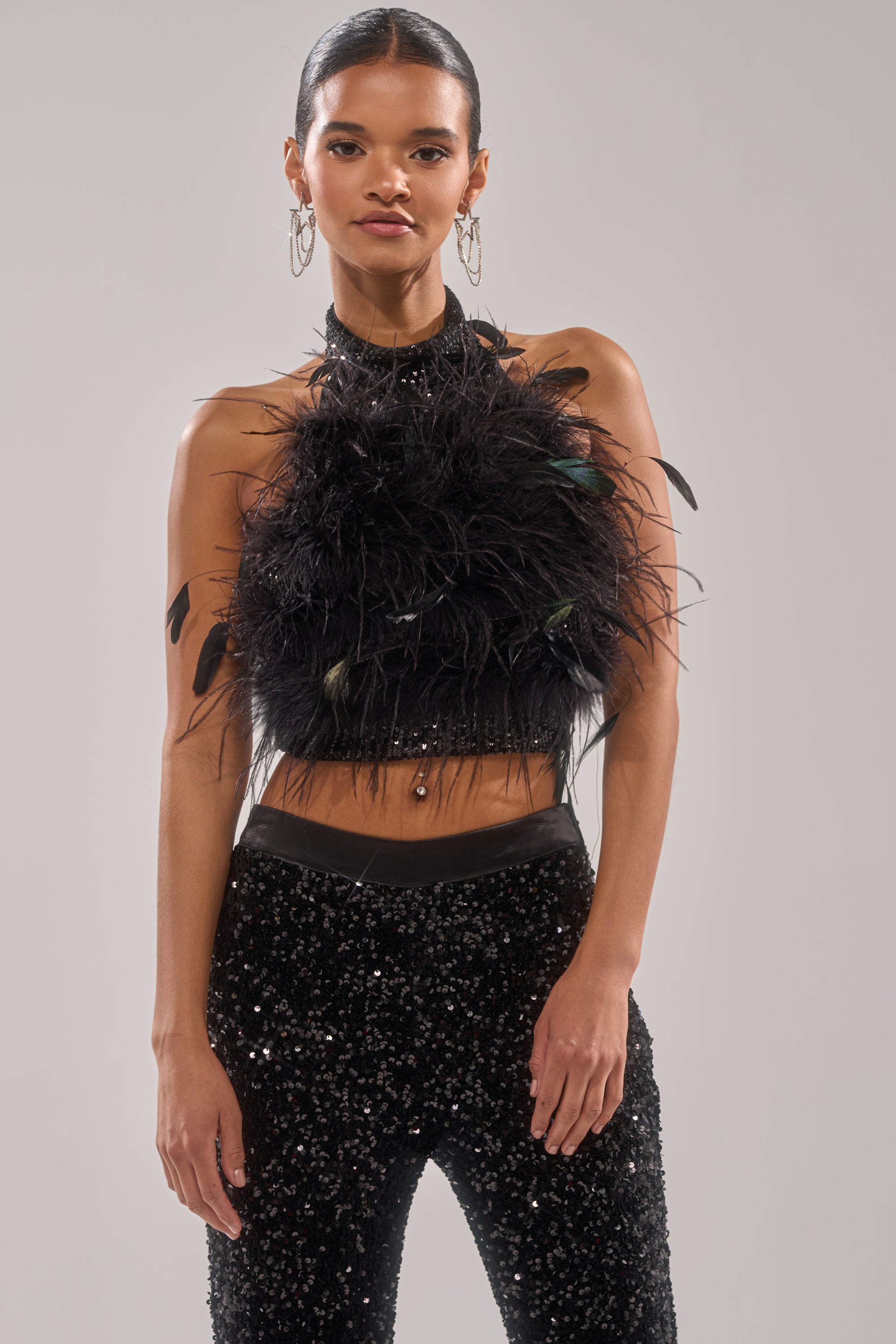 A woman wearing the FEATHER BABY BLOUSE and black sequin pants stands against a plain background, gazing at the camera with her hair pulled back and large hoop earrings. 1