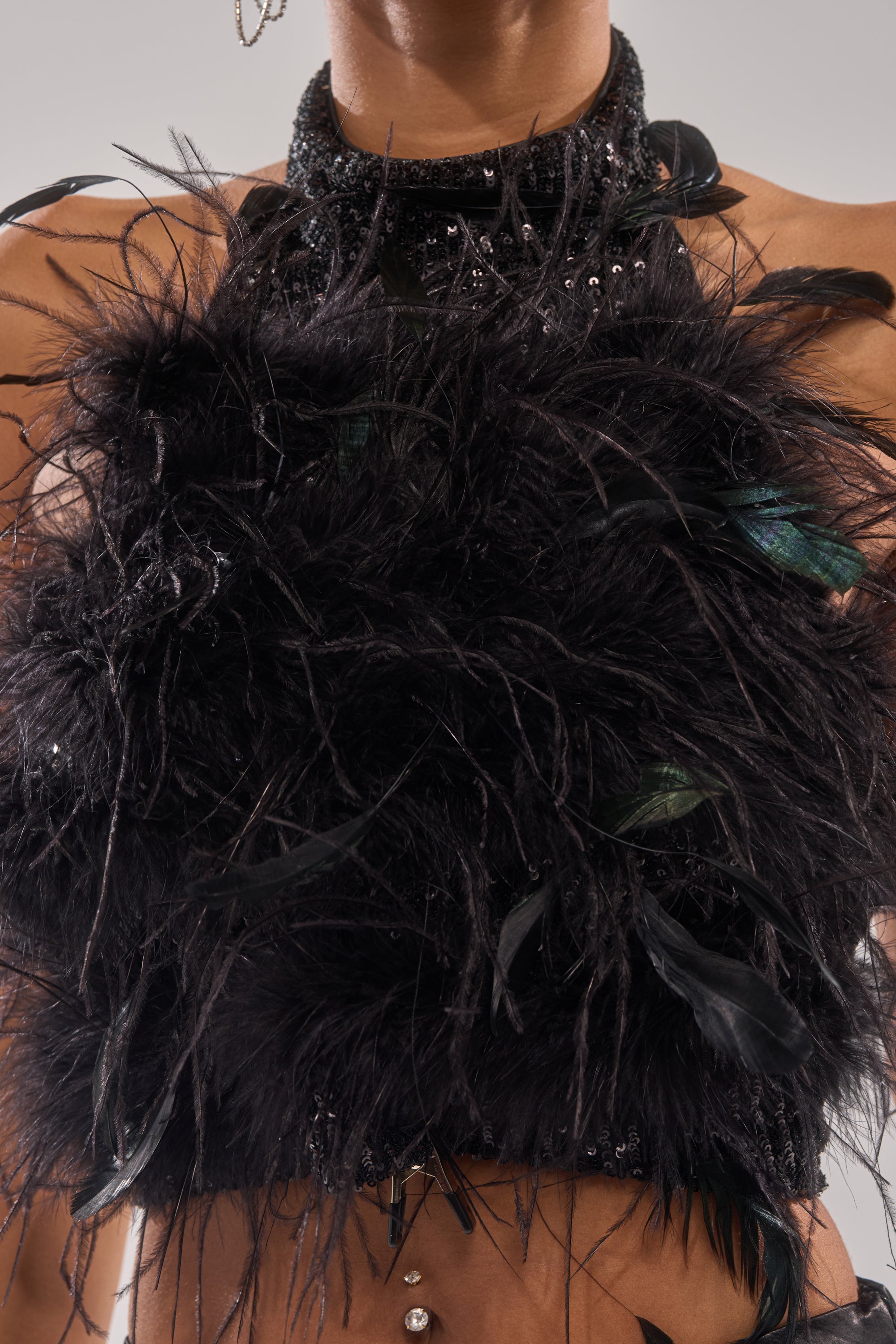 A person wearing the FEATHER BABY BLOUSE—a black sequin top with feathers, halter neckline, visible belly piercing, and bare arms. 6