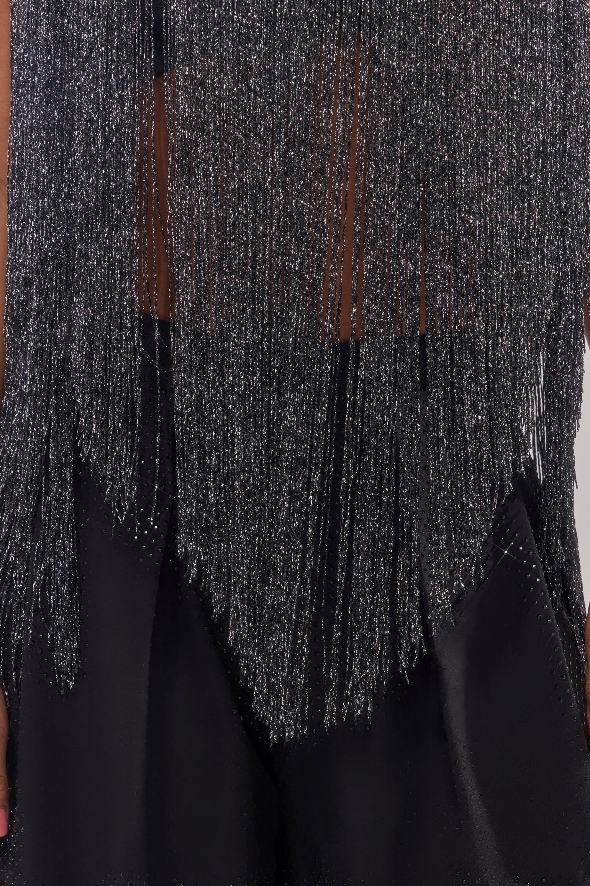 Close-up of the DEVVON FRINGE TOP, featuring long silver metallic fringe over sheer fabric. Black pants are visible underneath, and the fringe creates a shimmering, textured effect. 9