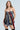 A woman with long hair wears the STRICTLY BUSINESS TIE DETAIL CORSET TOP, a unique business-casual dress crafted from diverse neckties in stripes and floral patterns. She stands against a plain, light-colored background.