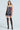 A woman stands against a light background in a STRICTLY BUSINESS TIE DETAIL CORSET TOP and strapless dress paired with black thigh-high stockings and studded heels, offering an eclectic twist on business casual attire.