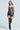 A woman poses in the STRICTLY BUSINESS TIE DETAIL CORSET TOP, made from colorful neckties with various patterns. She pairs it with black thigh-high stockings and patterned high heels, against a plain, light background.