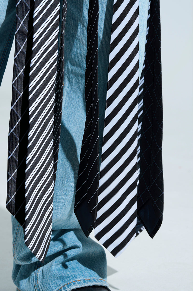 Wearing an ALL WORK AND NO PLAY TIE DETAIL CORSET TOP and blue jeans, a person showcases a collection of black and white neckties with designs such as diagonal stripes, checks, and grid patterns hanging stylishly down the leg for a business casual vibe.