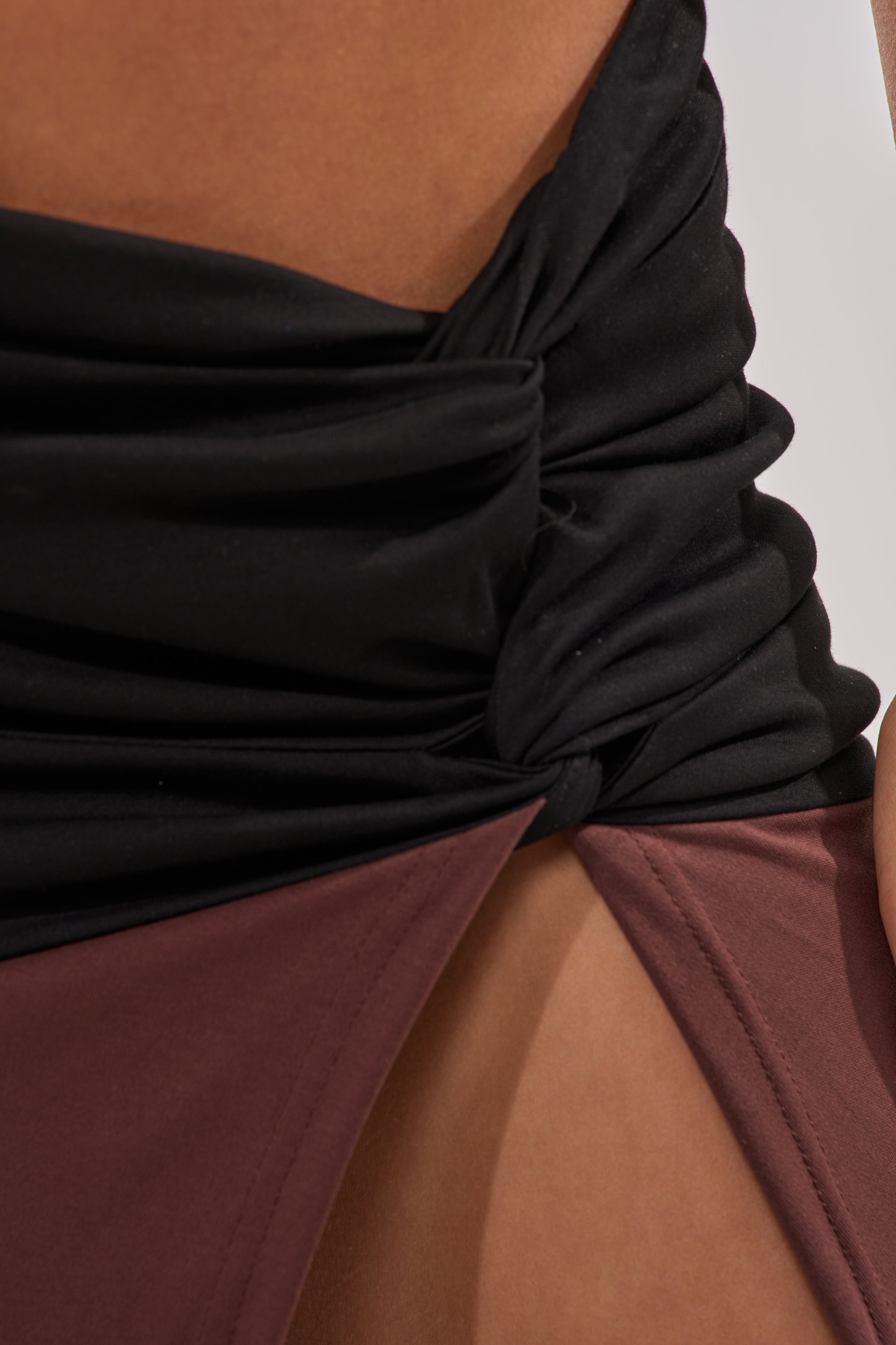 Close-up of a person wearing a black ruched top and the SCHOOL SPIRIT REWORKED MIDI SKIRT in brown, featuring a high-rise wrap front, high slit at the hip, and gathered, knotted detailing at the center for added texture. 9