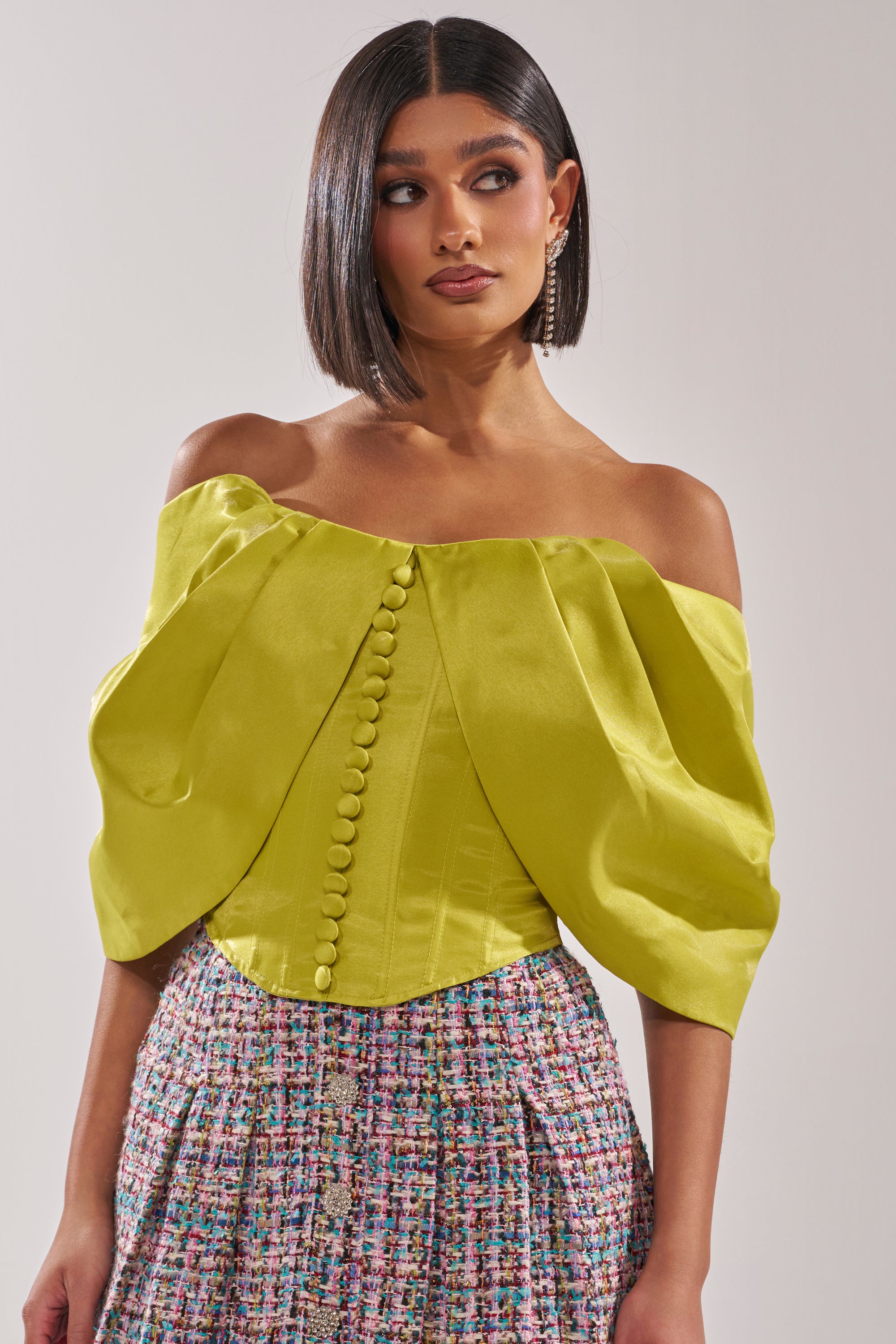A woman showcases the ELECTRIC CORSET IN GREEN with a high-waisted, multicolored textured skirt, channeling a couture-inspired silhouette. She has a sleek bob and gazes to the side. 2