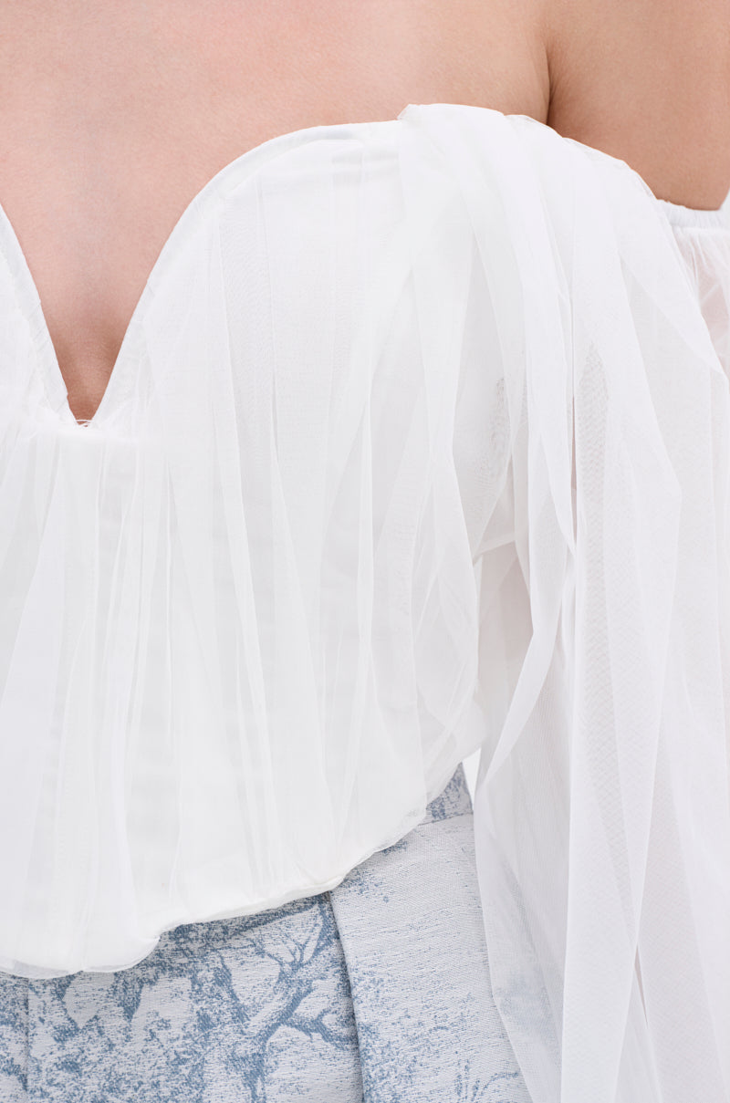 Close-up of a woman's upper body wearing the FLY WITH ME CORSET TOP IN WHITE, featuring an off-shoulder tulle design and sweetheart neckline. Styled with high-waisted, light blue and white patterned fabric against a neutral background.